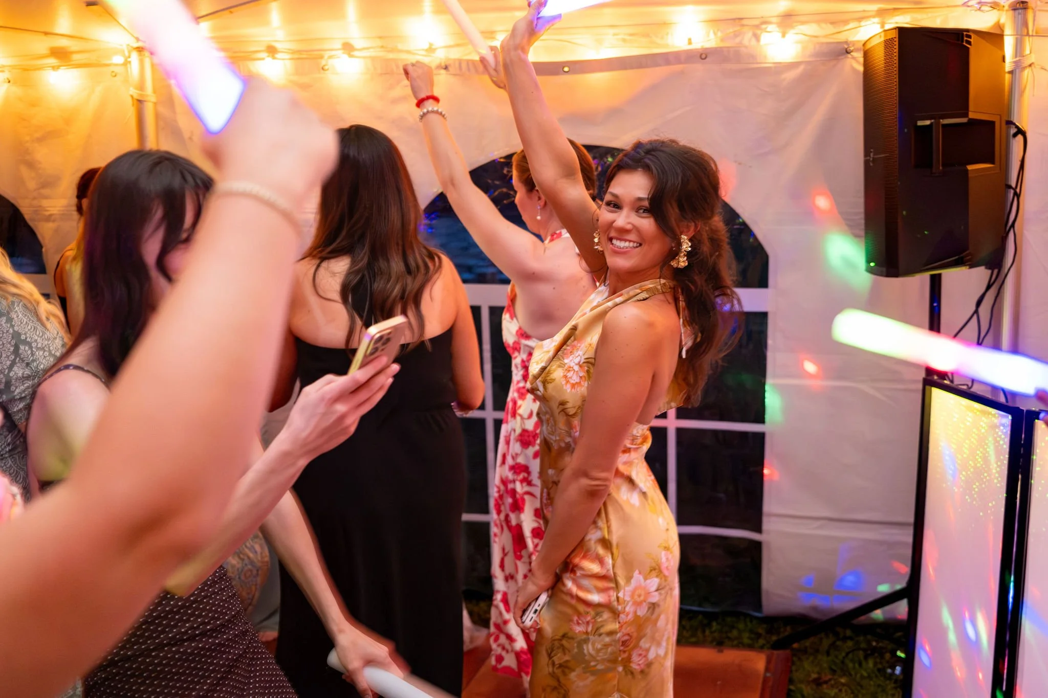 A guest dancing with glow sticks raised under the tent lights at Kayla and Ethan DeAngelis's Sanbornton New Hampshire wedding photography VMG Productions