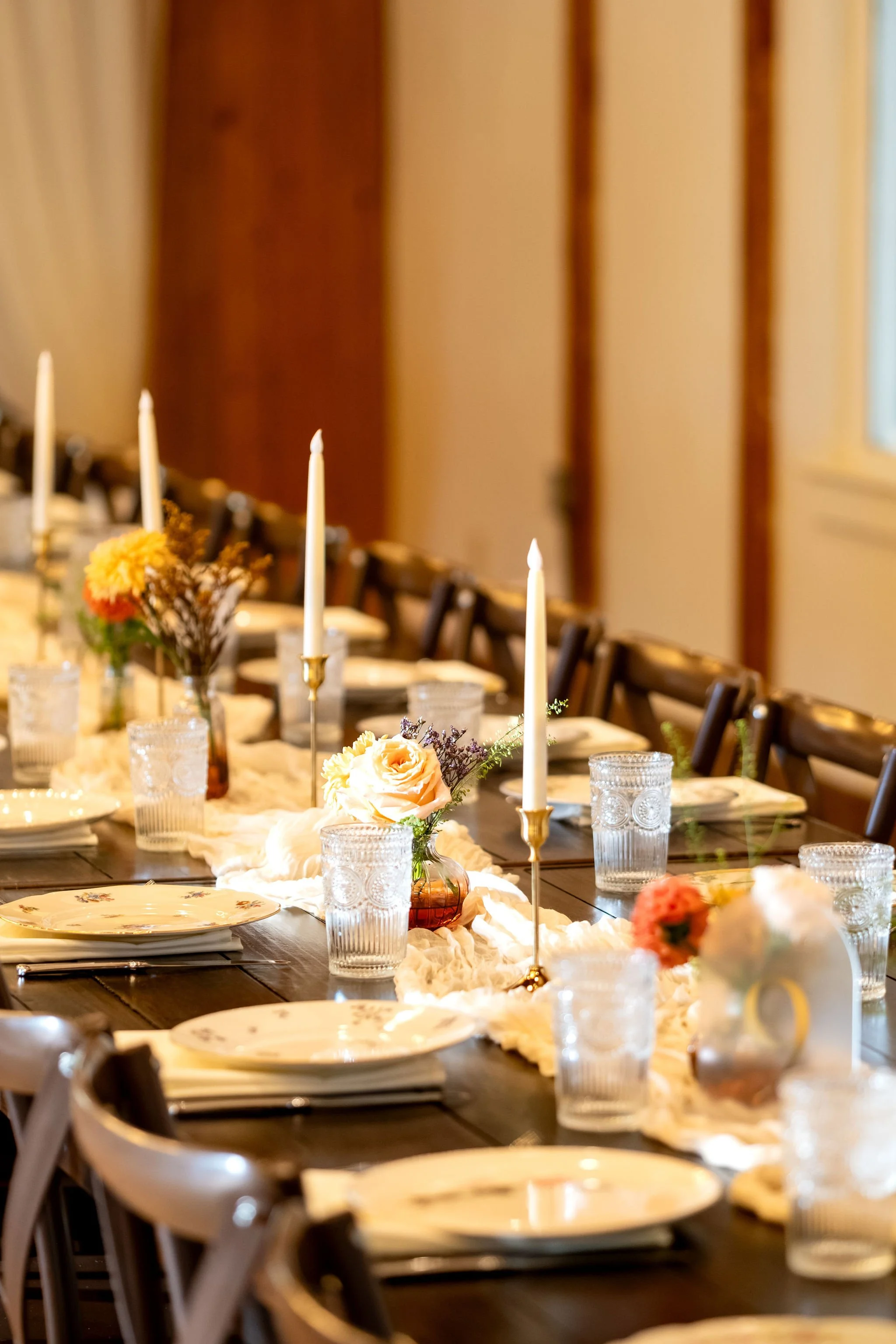 Long wooden table set with tall candles, flowers in burnt orange and peach, and floral china at Boothbay Playhouse in Boothbay Maine fall wedding photography VMG Productions
