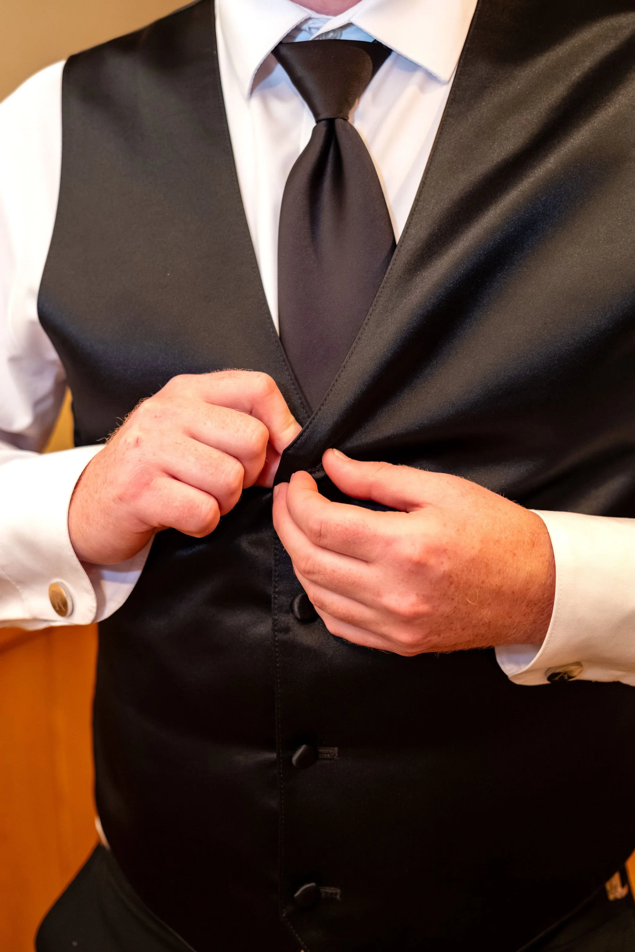 Alyssa and Colby close detail of the groom buttoning his black vest with monogrammed cufflinks in Bethel Maine summer wedding photography VMG Productions