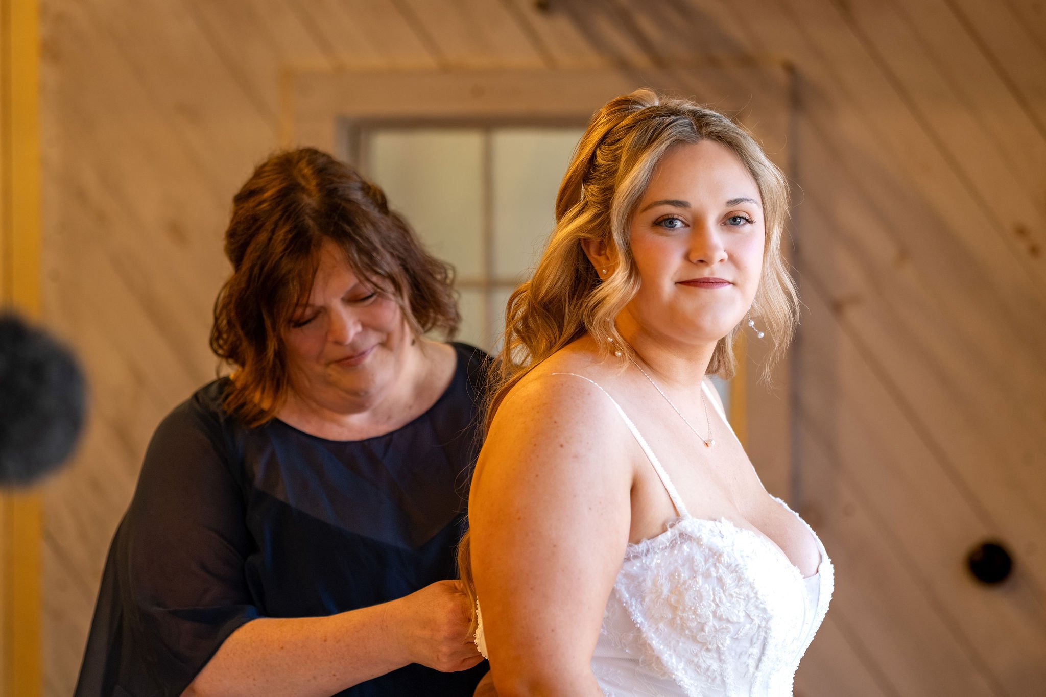 Ellie looking over her shoulder as her mom fastens the back of her dress at Boothbay Playhouse in Boothbay Maine fall wedding photography VMG Productions