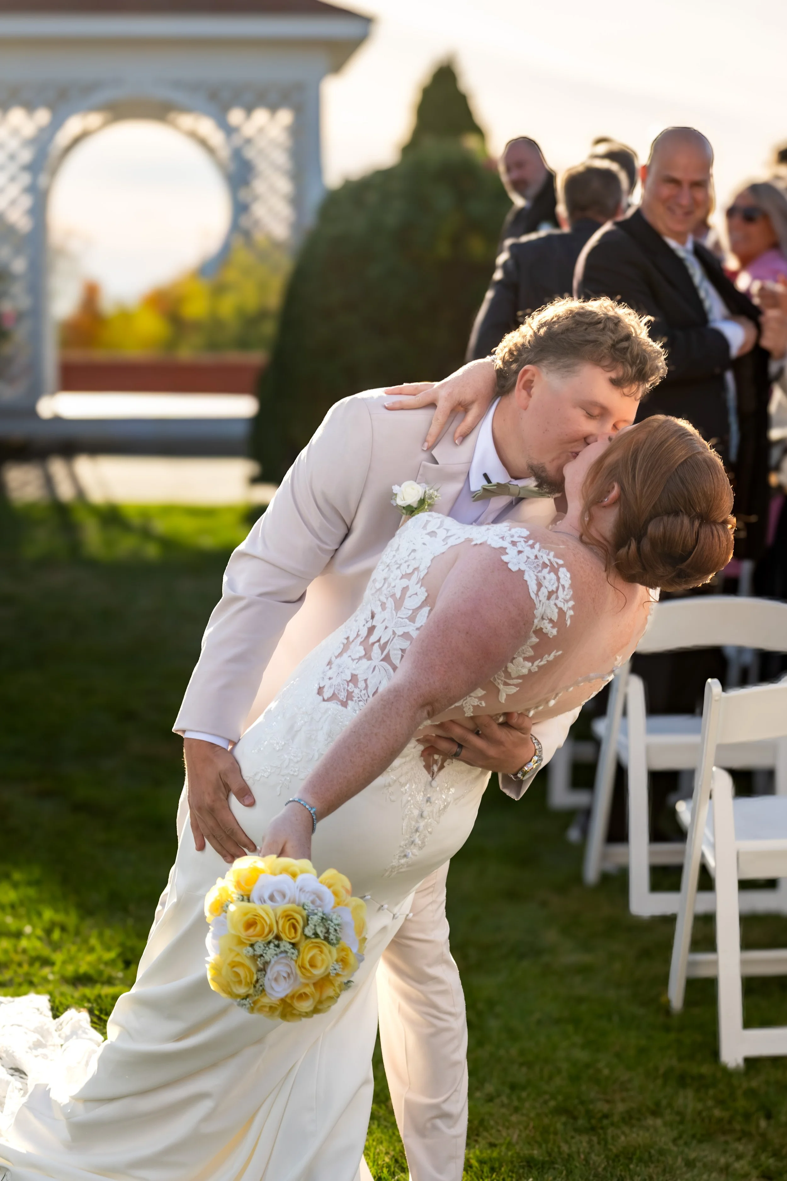 Andrew dipping Erika for a kiss on the ceremony lawn with her yellow bouquet in hand at the Maine Wedding Barn and Event Center in Minot Maine fall wedding photography VMG Productions