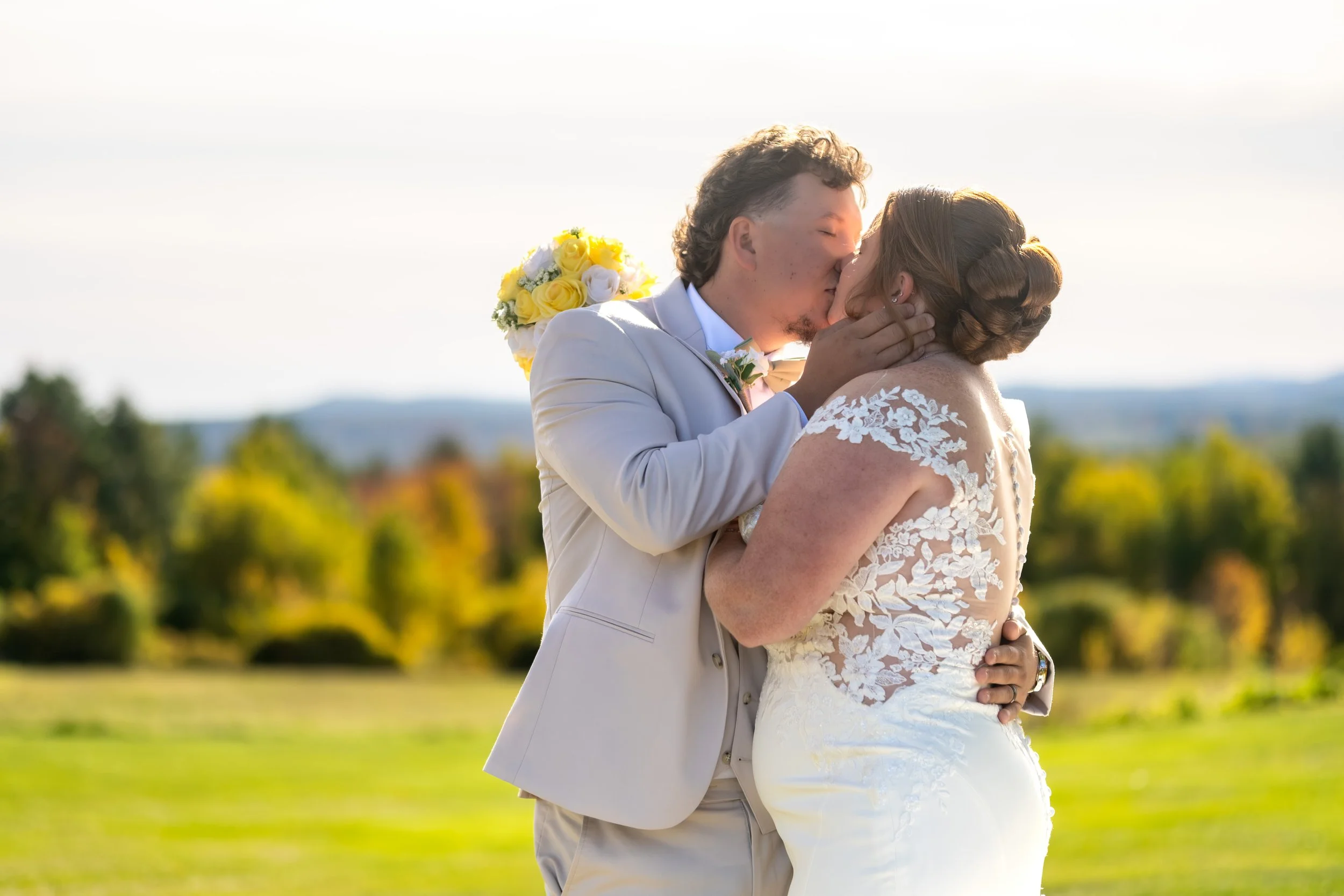 Andrew and Erika kissing on the lawn with the hills behind them at the Maine Wedding Barn and Event Center in Minot Maine fall wedding photography VMG Productions