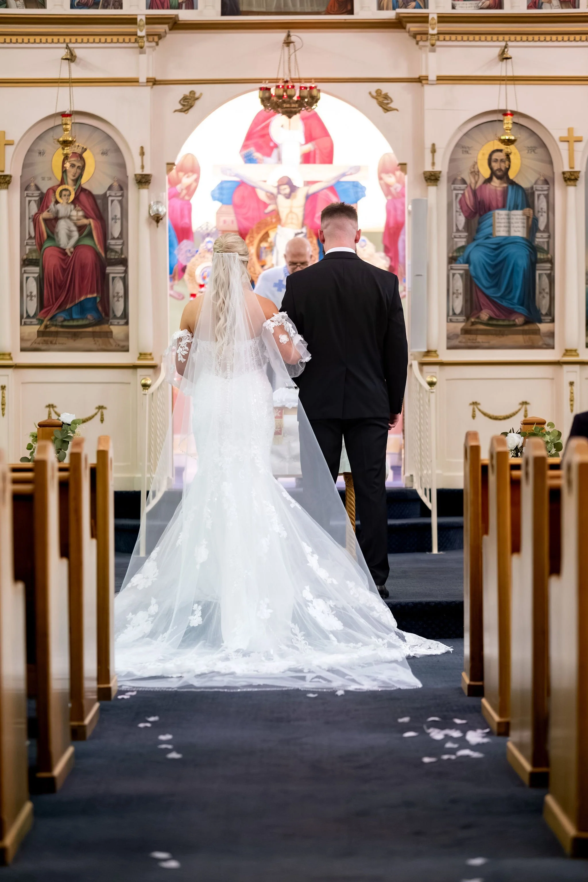 Jeremiah and Vienna centered aisle view of bride and groom standing before the altar during the ceremony at Holy Trinity Greek Orthodox Church Portland Maine spring wedding photography VMG Productions