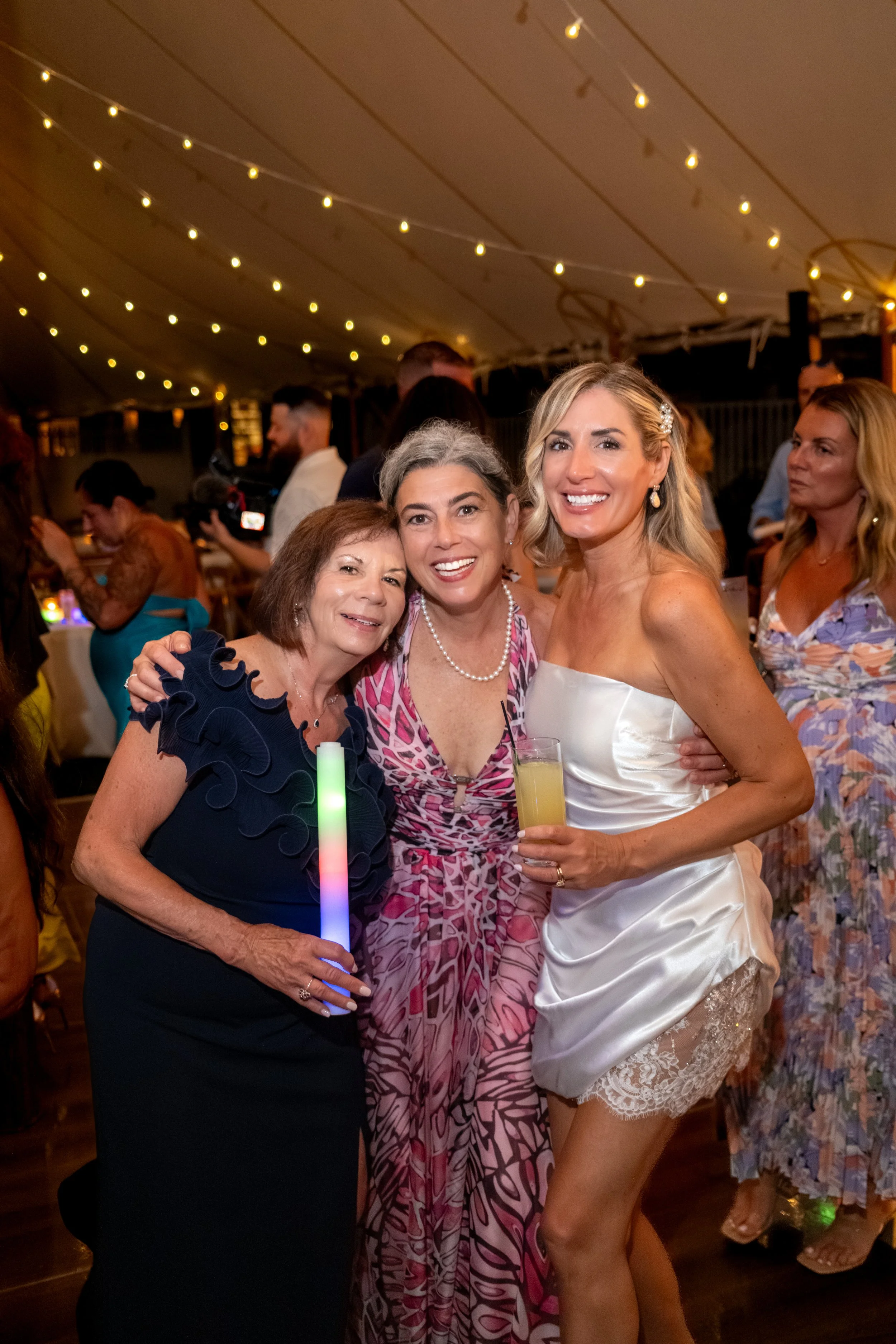 Ashley Draper in her lace trimmed second dress with guests under the tent lights at The Breakwater Inn in Kennebunkport Maine summer wedding photography VMG Productions