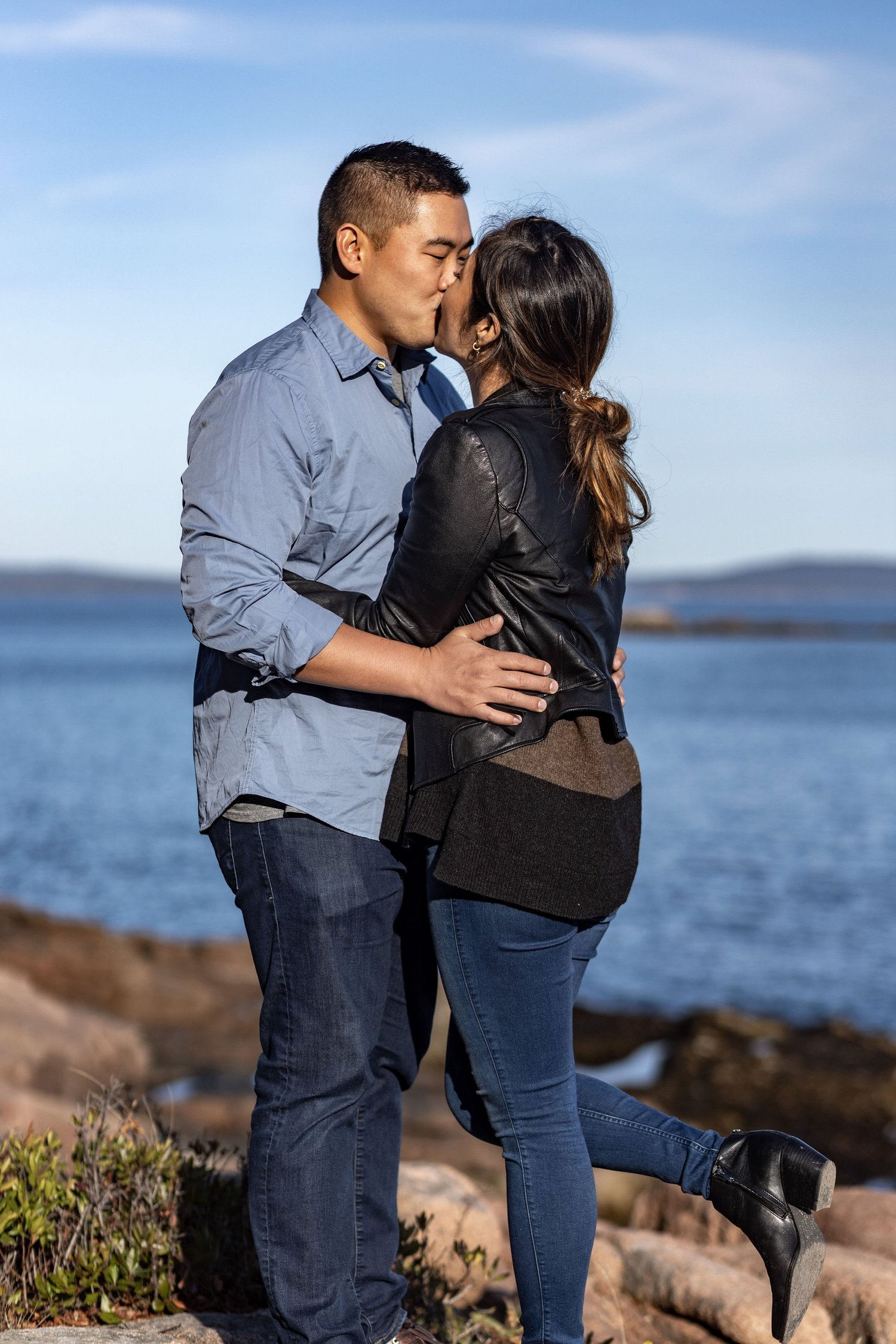 Agnes and Peter kissing standing on coastal rocks ocean behind Acadia National Park engagement VMG Productions