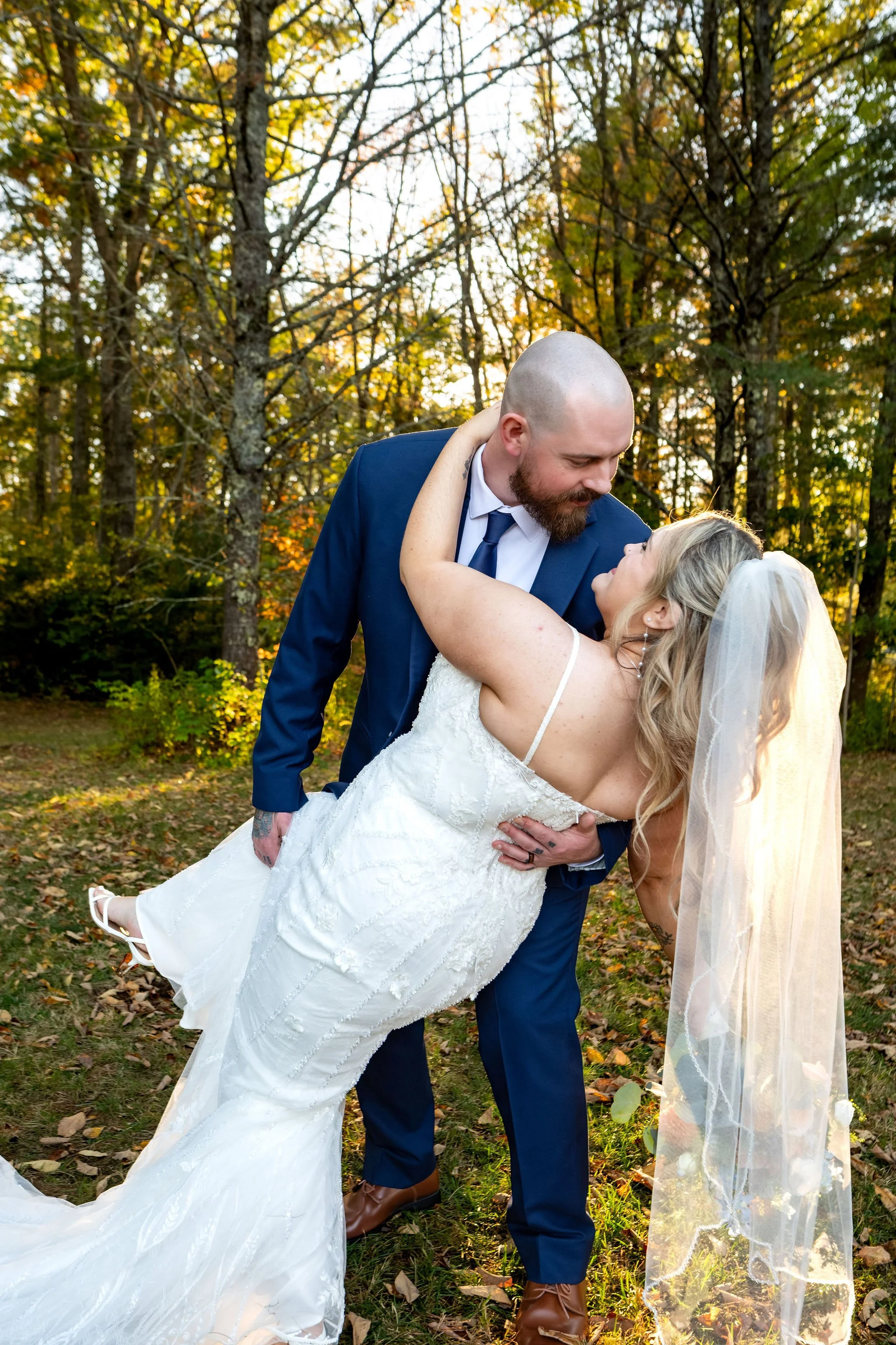 Sam dipping Ellie for a kiss with her veil and train sweeping toward the ground at Boothbay Playhouse in Boothbay Maine fall wedding photography VMG Productions