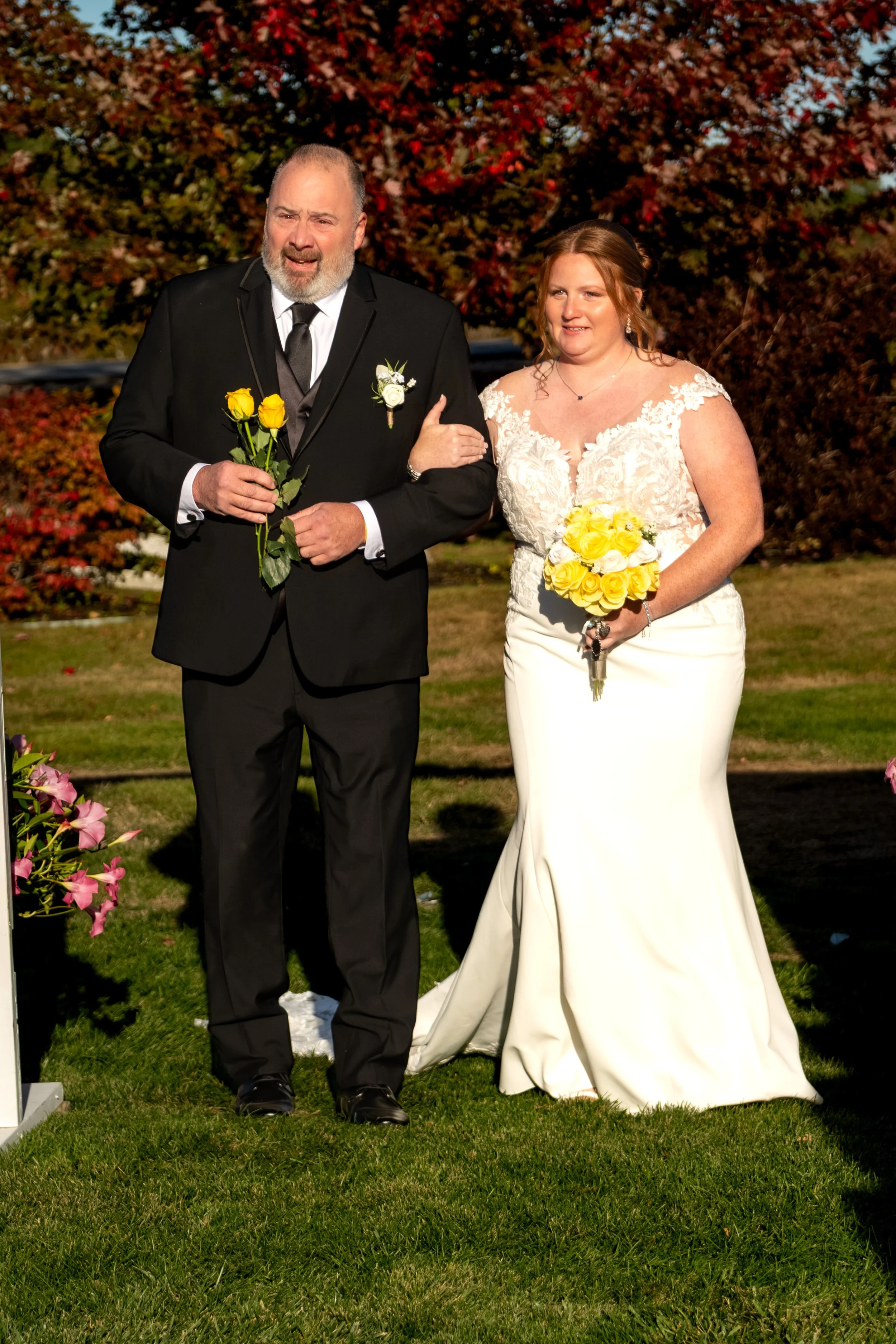 Erika with her dad in front of red maple trees, both holding yellow roses at the Maine Wedding Barn and Event Center in Minot Maine fall wedding photography VMG Productions