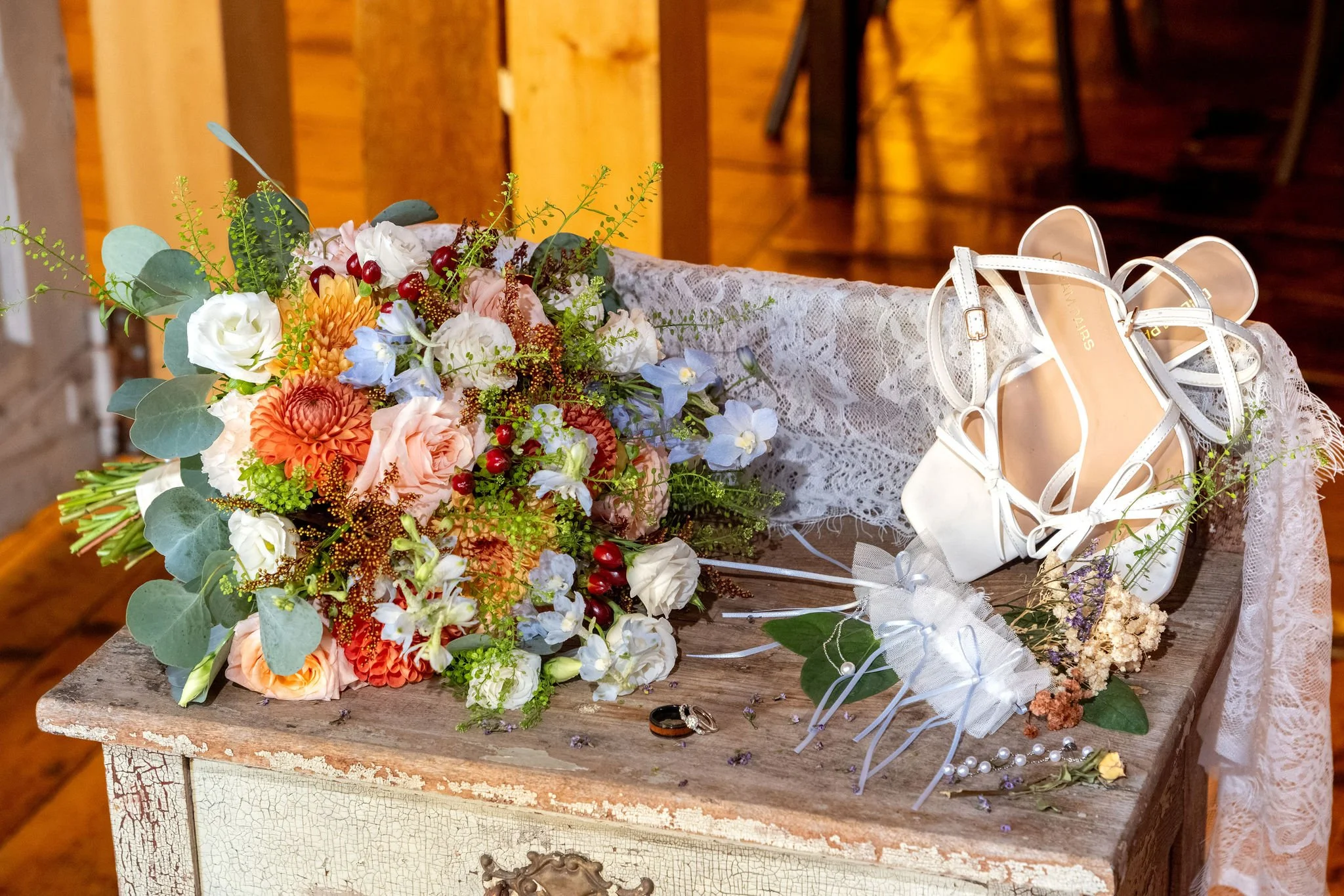 Ellie's bouquet of burnt orange, peach, and dusty blue flowers on a rustic chest beside her white heels at Boothbay Playhouse in Boothbay Maine fall wedding photography VMG Productions