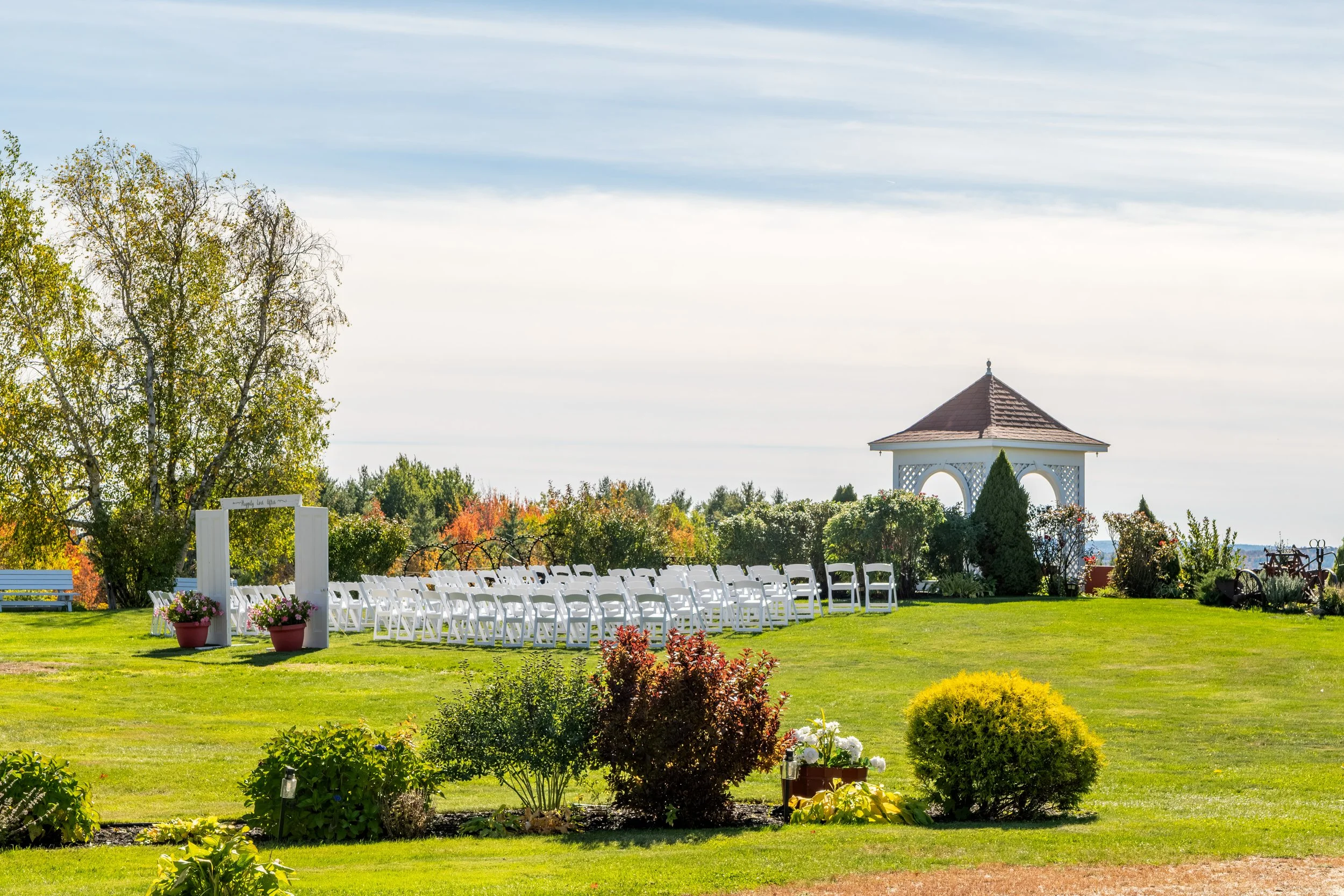 The ceremony lawn with white chairs and a gazebo set among fall trees at the Maine Wedding Barn and Event Center in Minot Maine fall wedding photography VMG Productions