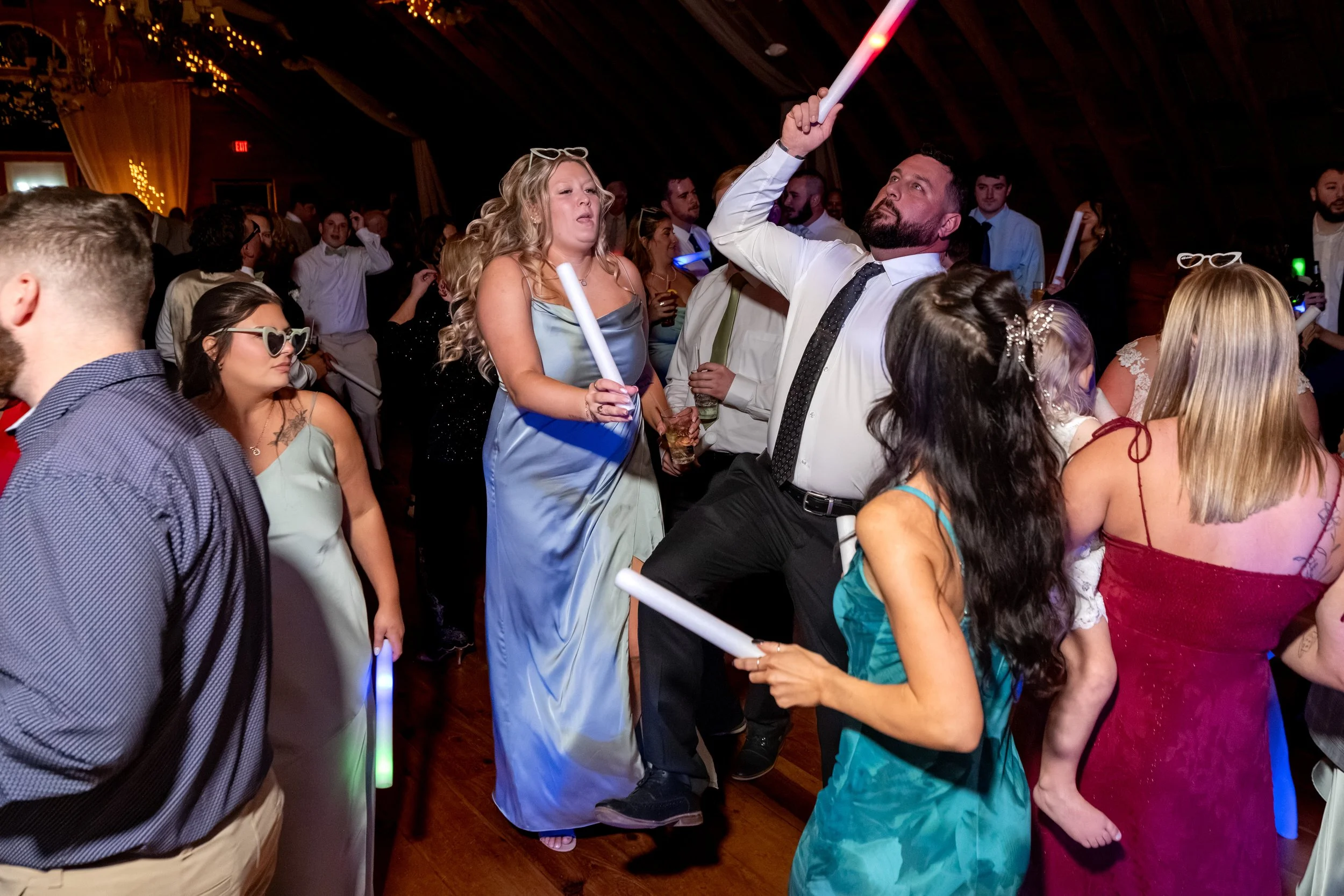 Guests dancing under the barn's string lights with light-up wands raised at the Maine Wedding Barn and Event Center in Minot Maine fall wedding photography VMG Productions