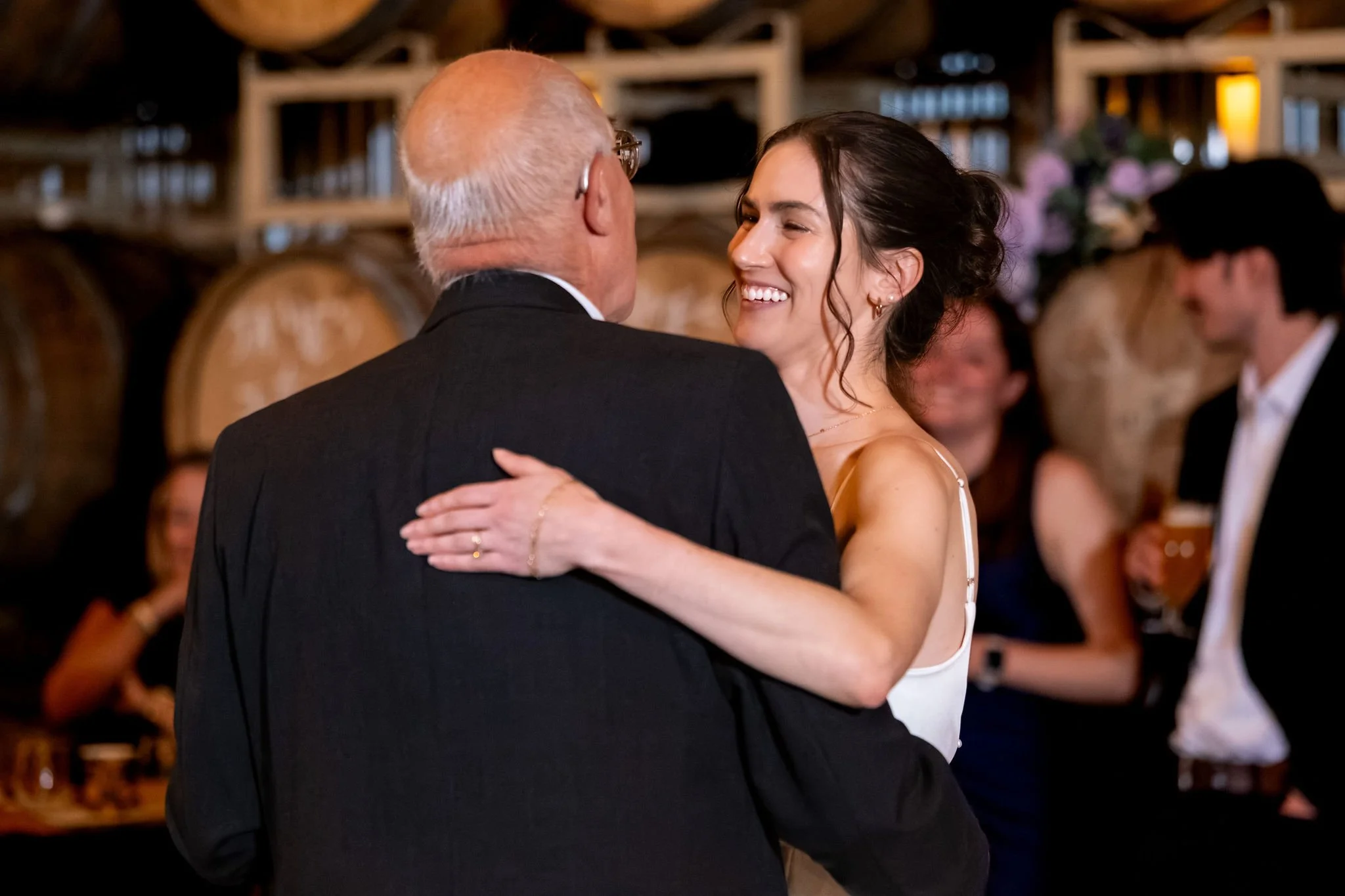 Victoria smiling over her dad's shoulder during their father daughter dance at The Cellars at Allagash Brewing Company in Portland Maine fall wedding photography VMG Productions