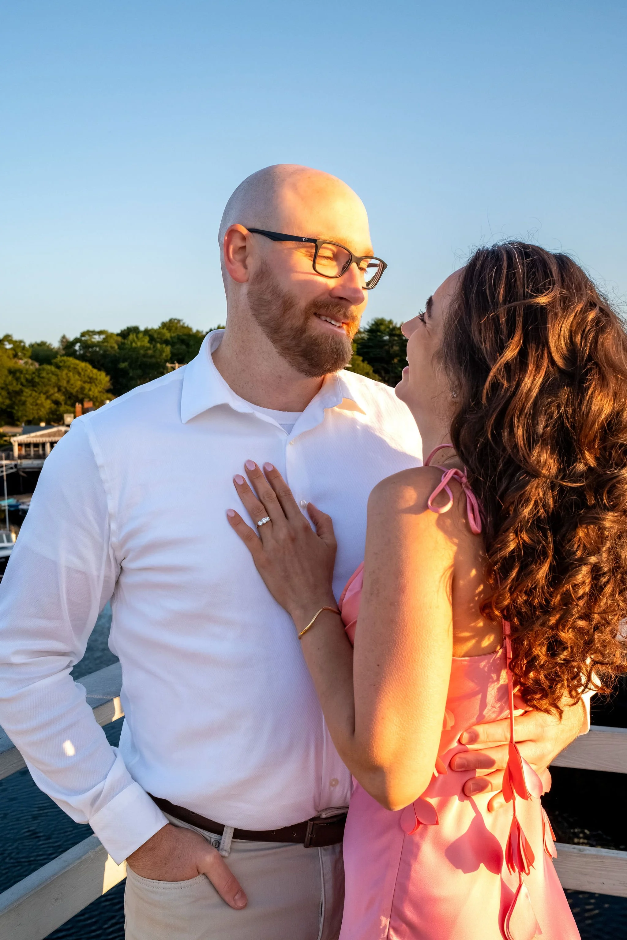 Helena laughing as she looks up at Zack with her hand on his chest and the ring showing on Marginal Way in Ogunquit Maine sunrise proposal and engagement photography VMG Productions