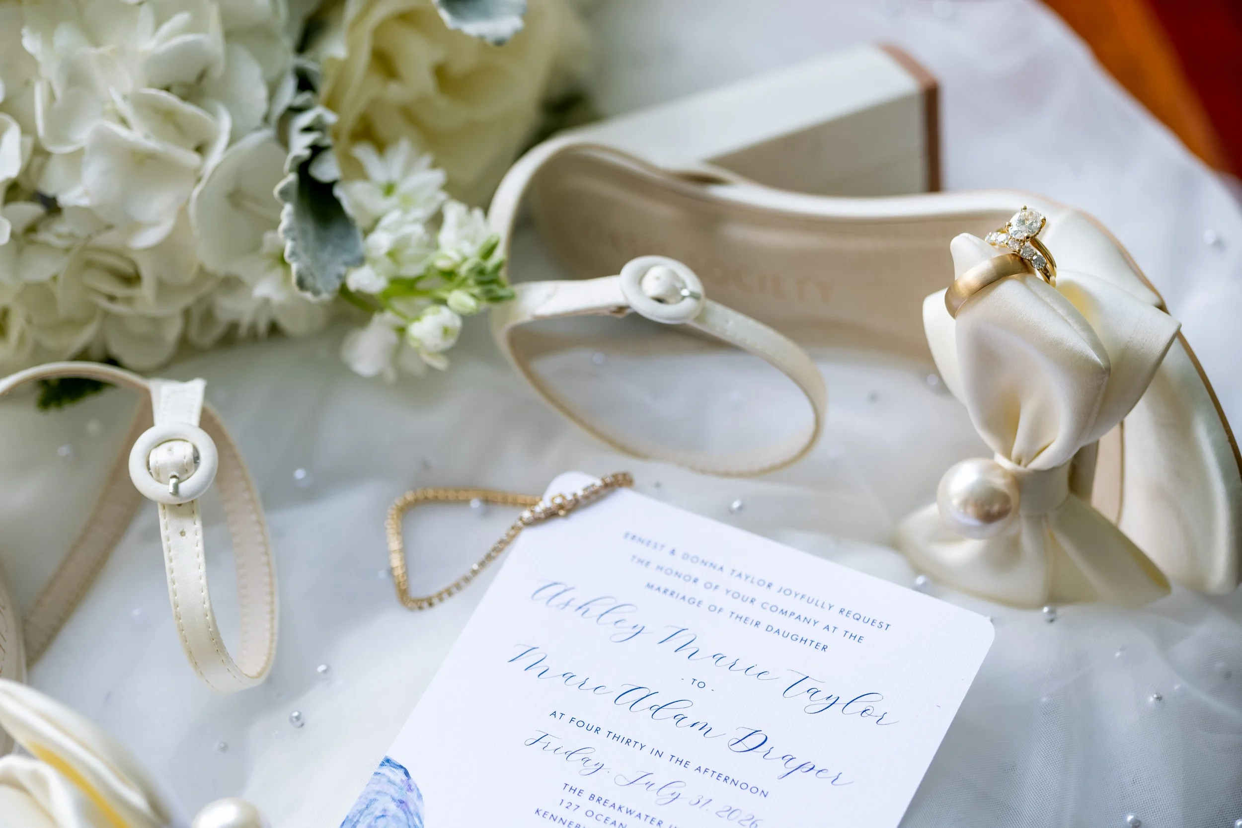 Ashley and Marc Draper's blue calligraphy wedding invitation styled with rings, heels, and jewelry at The Breakwater Inn in Kennebunkport Maine summer wedding photography VMG Productions