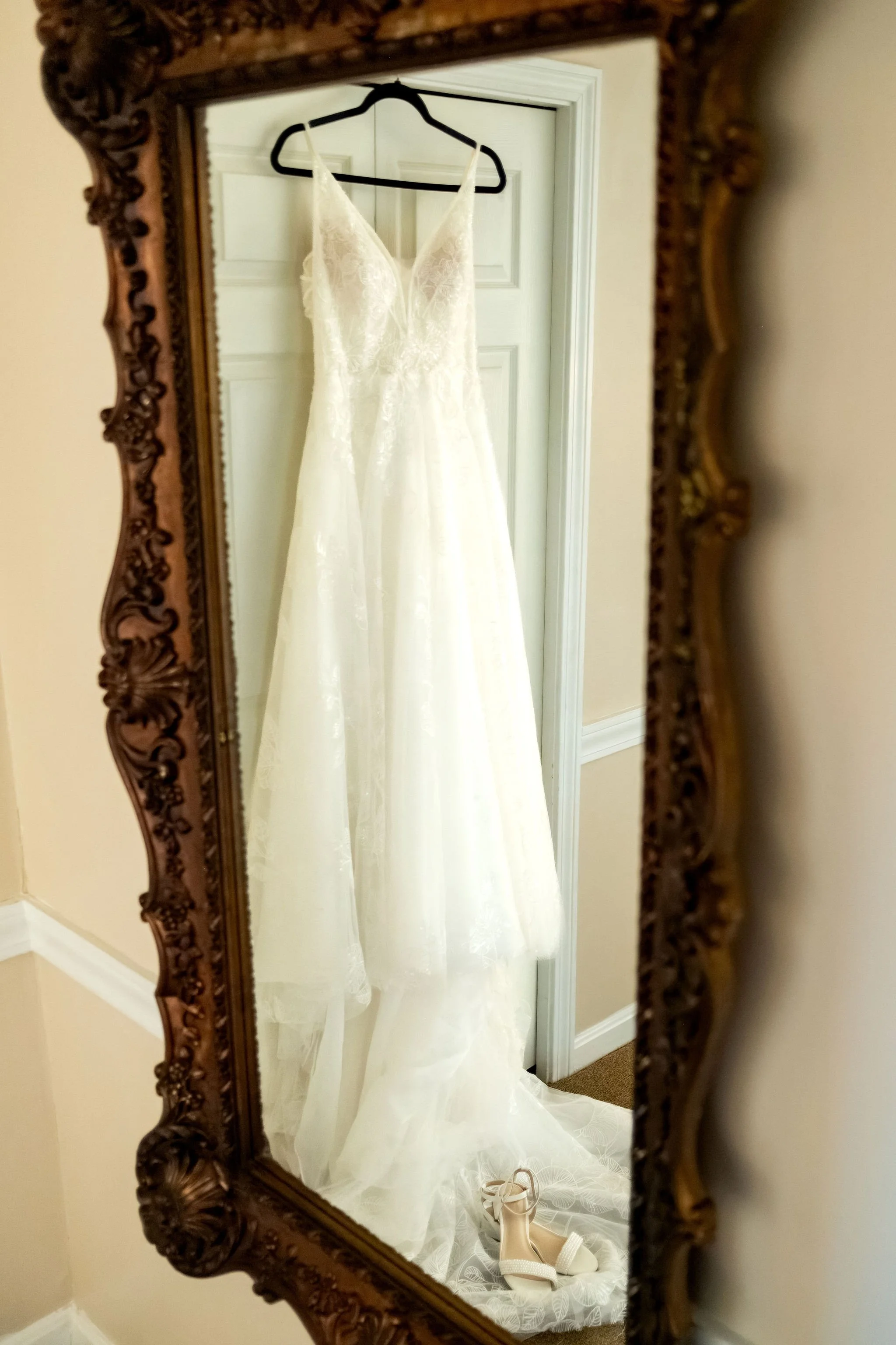 Hollie's lace wedding gown hanging on a door reflected in an ornate gold mirror at The Lucerne Inn in Dedham Maine summer wedding photography VMG Productions