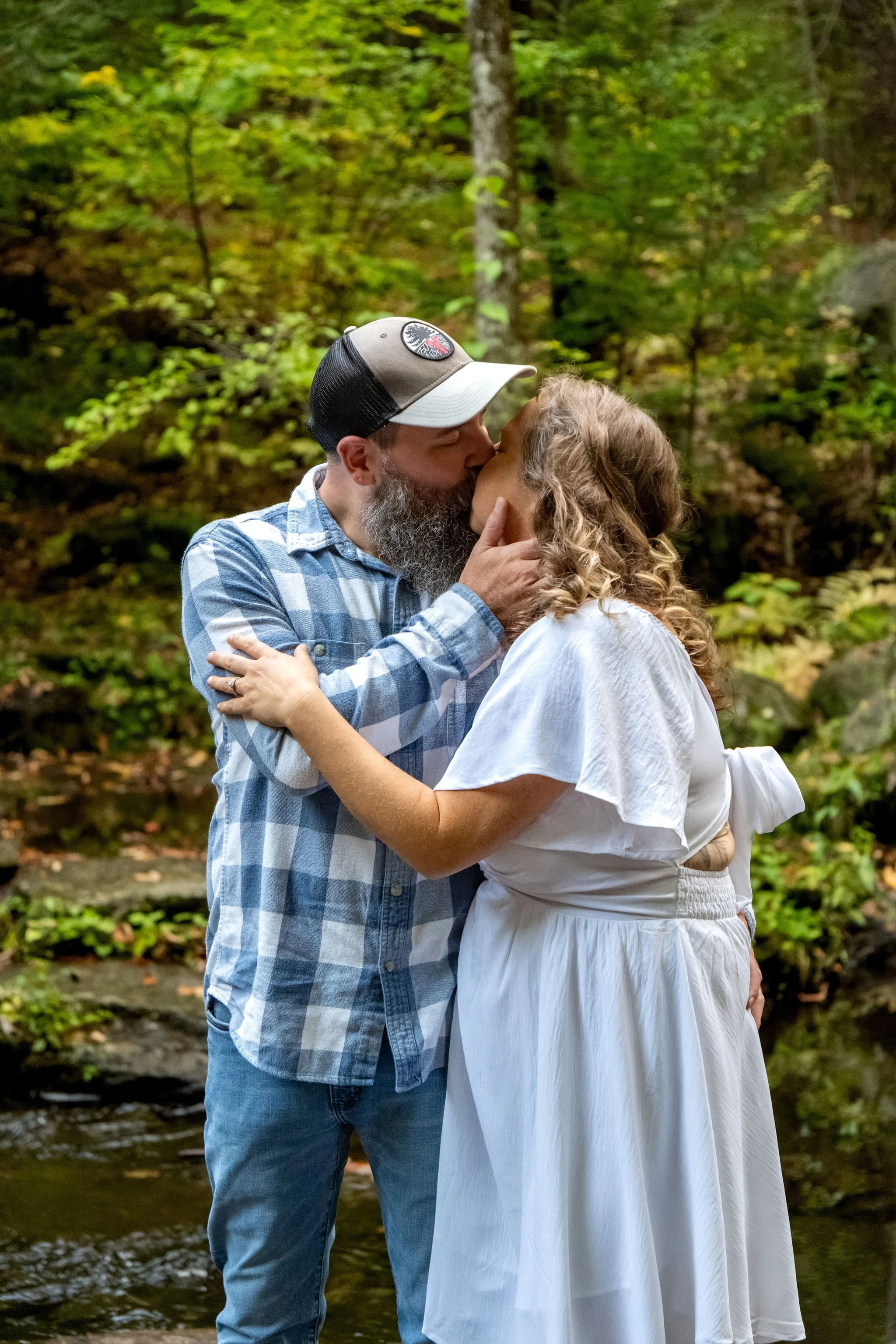 Alison and Dave kissing in front of the mossy stone wall with green and gold leaves behind them at Vaughan Woods in Hallowell Maine fall engagement photography VMG Productions