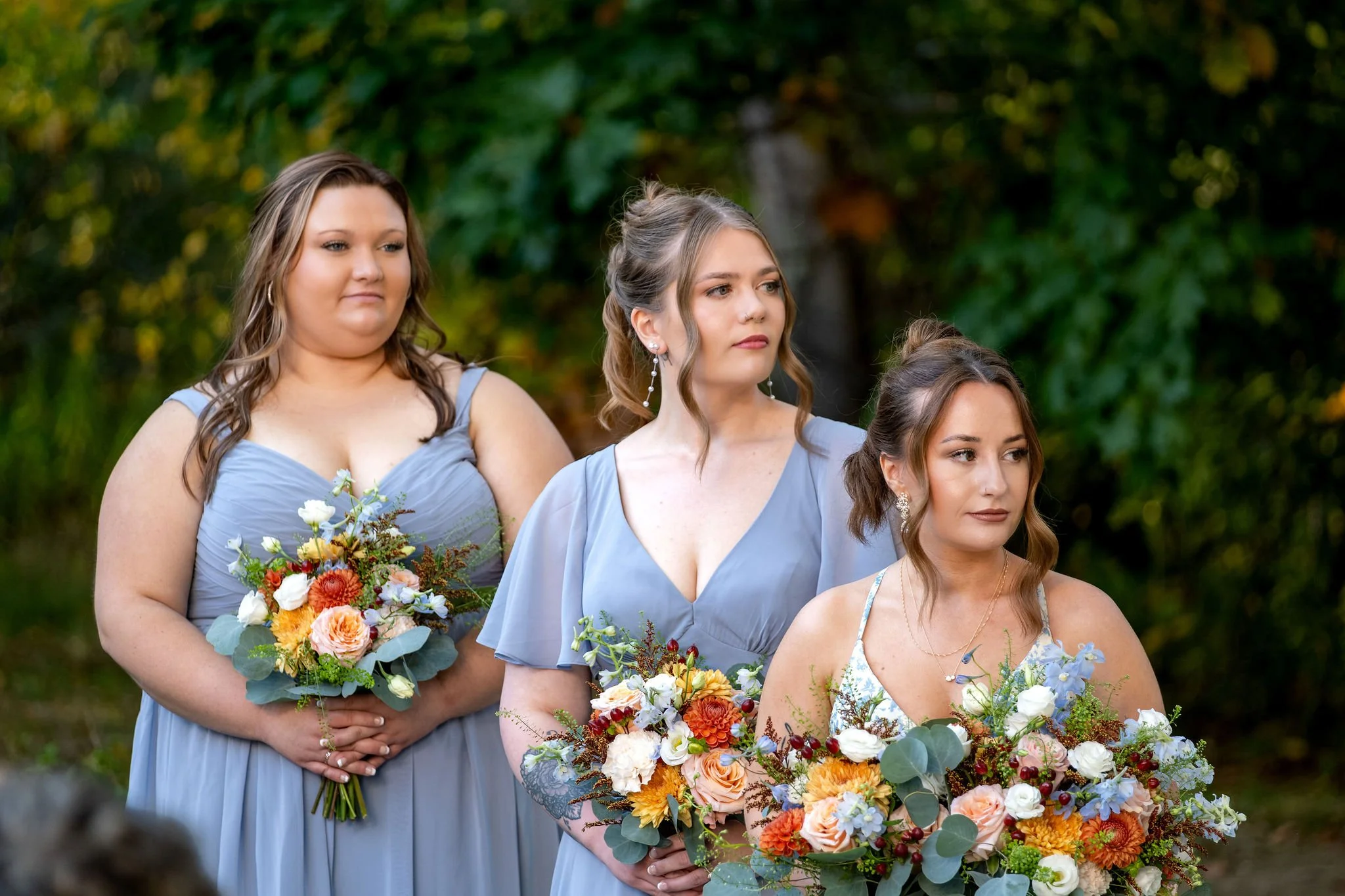 Ellie's bridesmaids in dusty blue dresses holding their bouquets as they watch the ceremony at Boothbay Playhouse in Boothbay Maine fall wedding photography VMG Productions