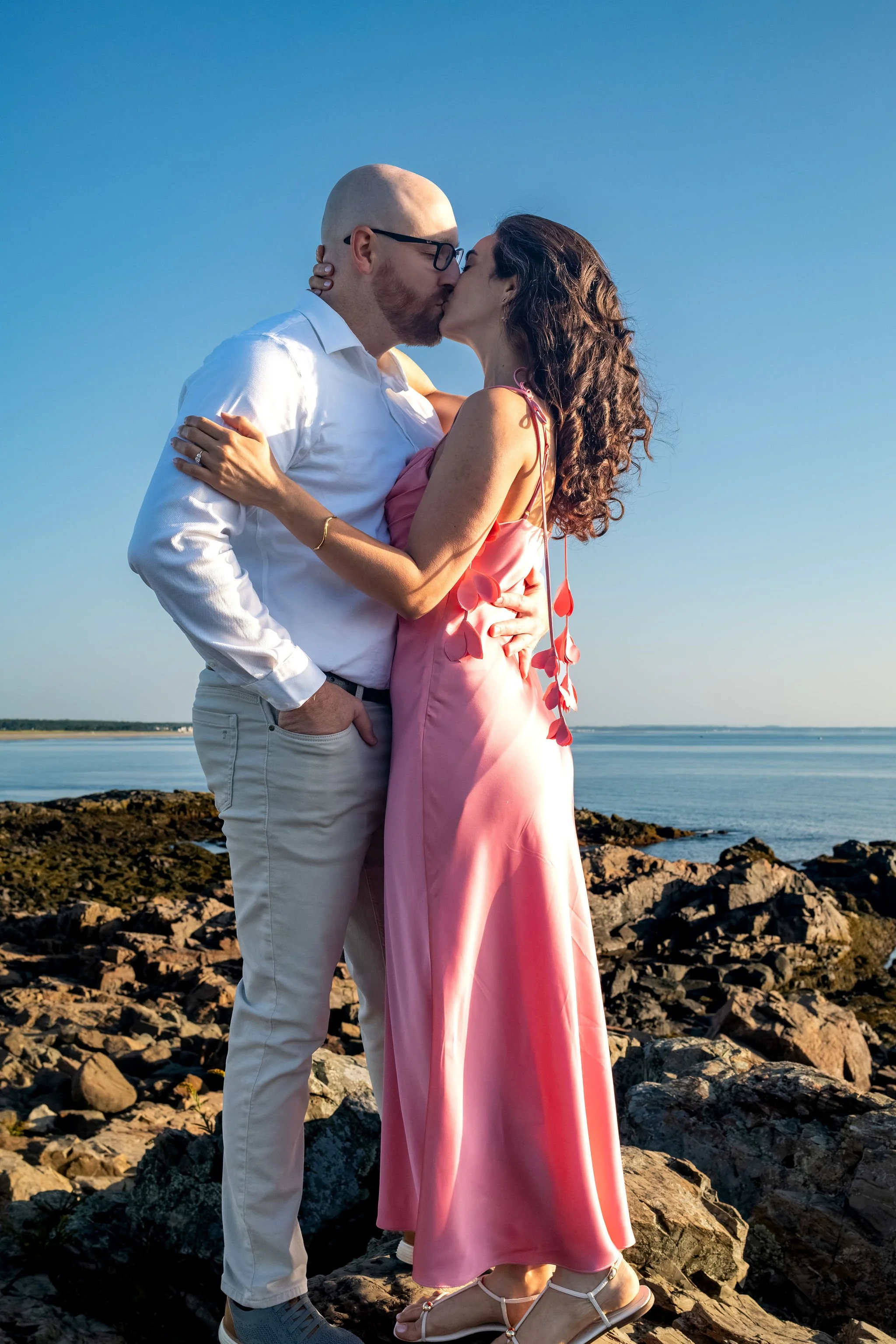 Zack and Helena kissing on the rocky shore with the ocean spreading out behind them on Marginal Way in Ogunquit Maine sunrise proposal and engagement photography VMG Productions