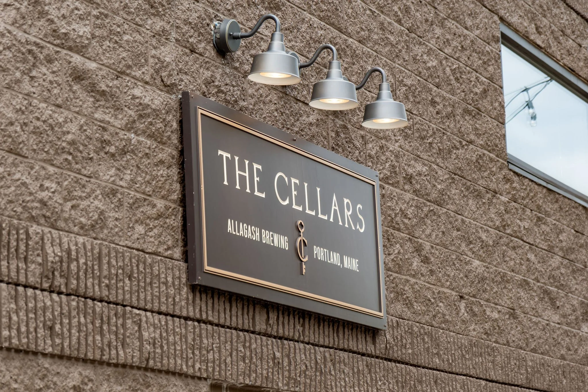 The Cellars at Allagash Brewing sign mounted on the building beneath three gooseneck lights at The Cellars at Allagash Brewing Company in Portland Maine fall wedding photography VMG Productions