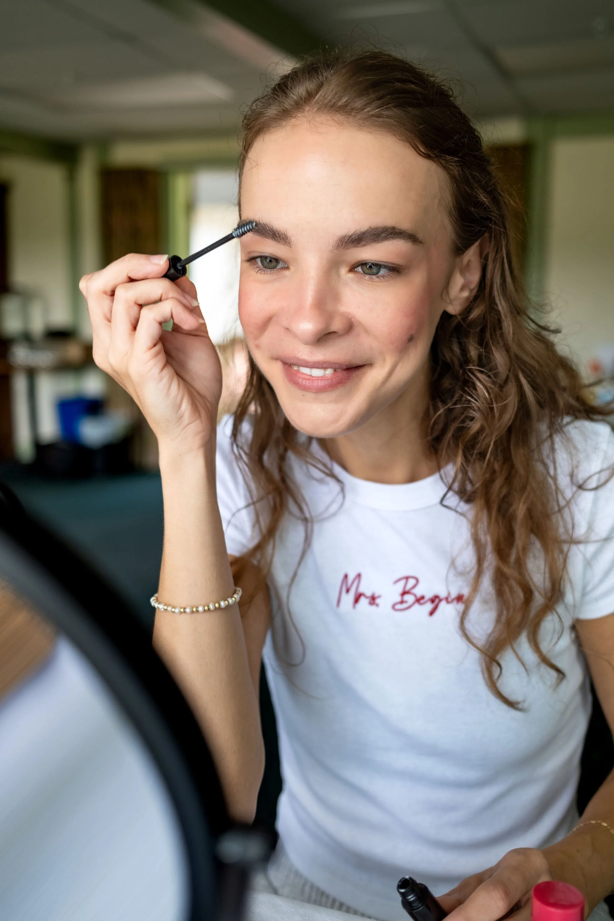 Cassidy Begin applying her own mascara in a round mirror while getting ready at Maple Hill Farm Inn and Conference Center in Hallowell Maine summer wedding photography VMG Productions
