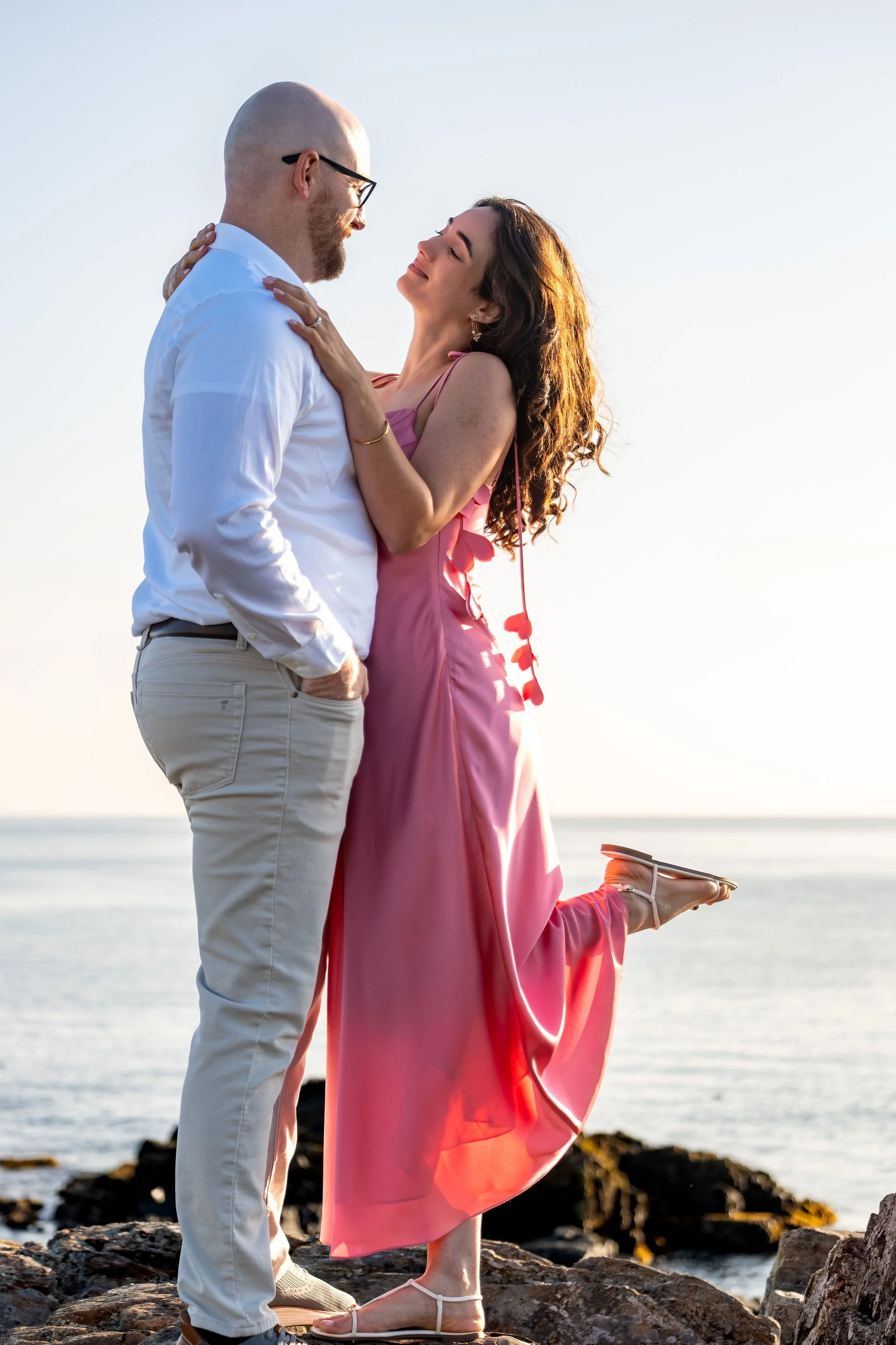 Helena looking up at Zack with a big smile and her foot kicked up behind her on Marginal Way in Ogunquit Maine sunrise proposal and engagement photography VMG Productions