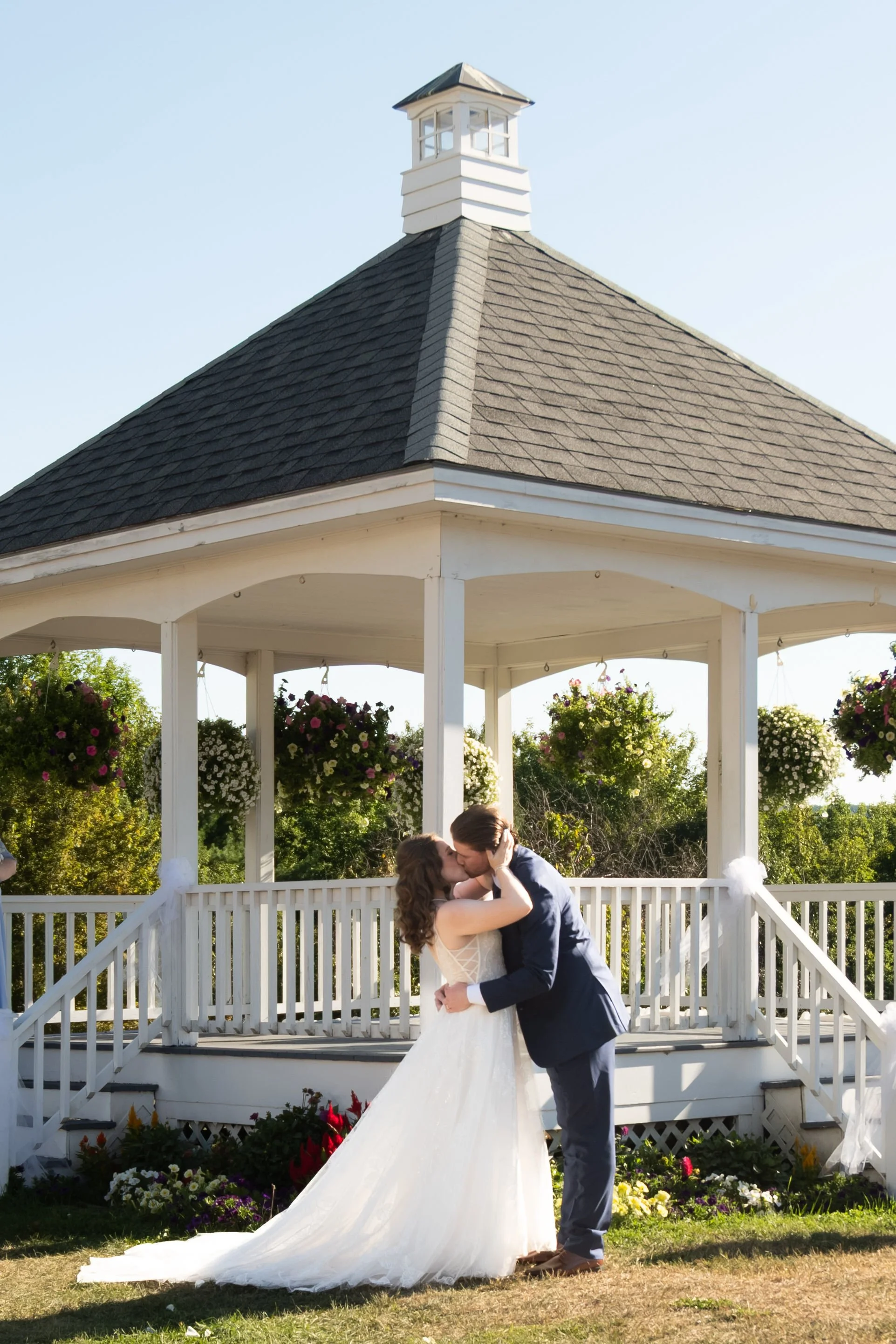 Zachary and Hollie's first kiss as a married couple beneath the white gazebo at The Lucerne Inn in Dedham Maine summer wedding photography VMG Productions