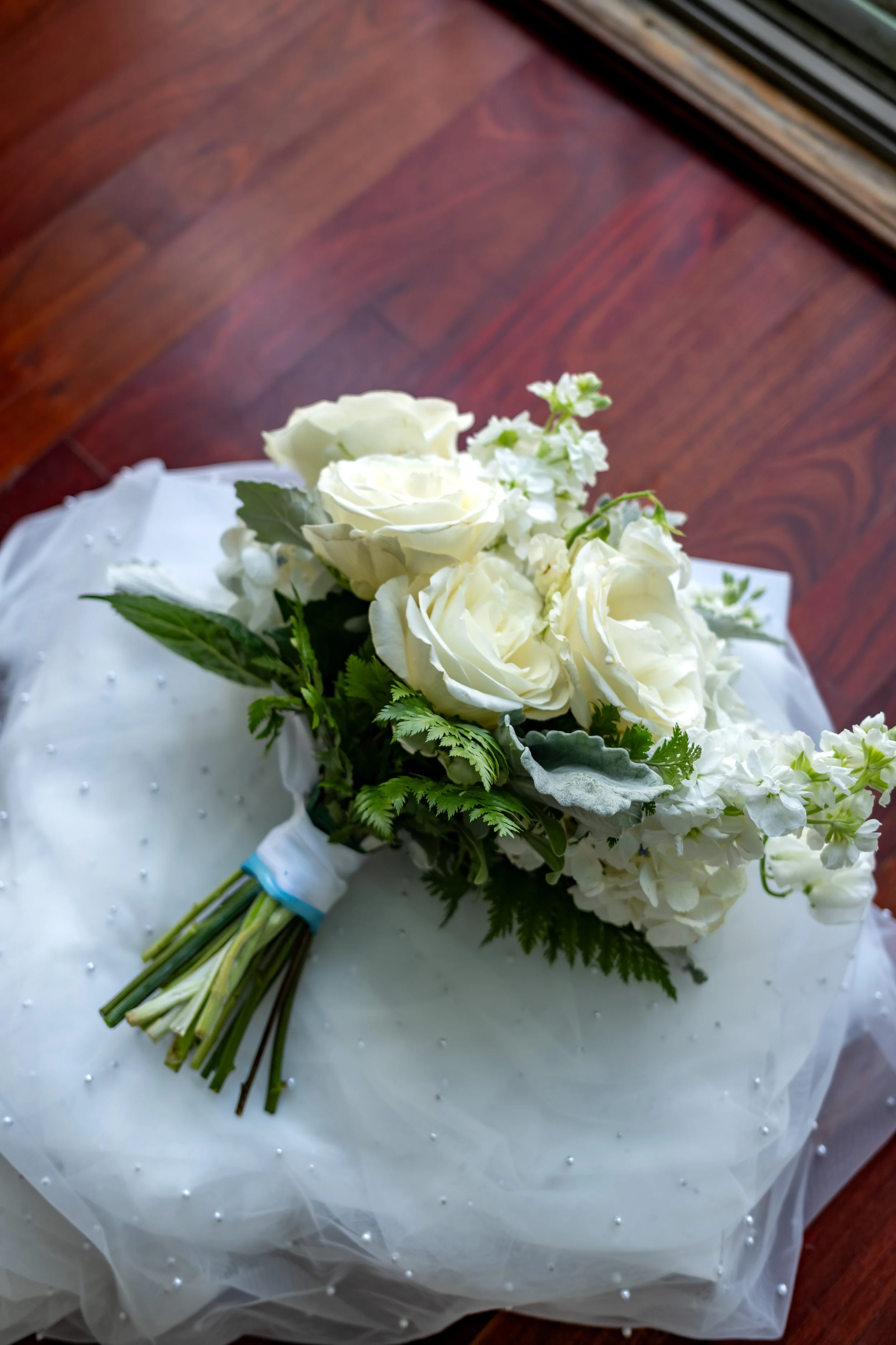 Ashley Draper's white rose bouquet by OffMill Flowers resting on her pearl veil at The Breakwater Inn in Kennebunkport Maine summer wedding photography VMG Productions