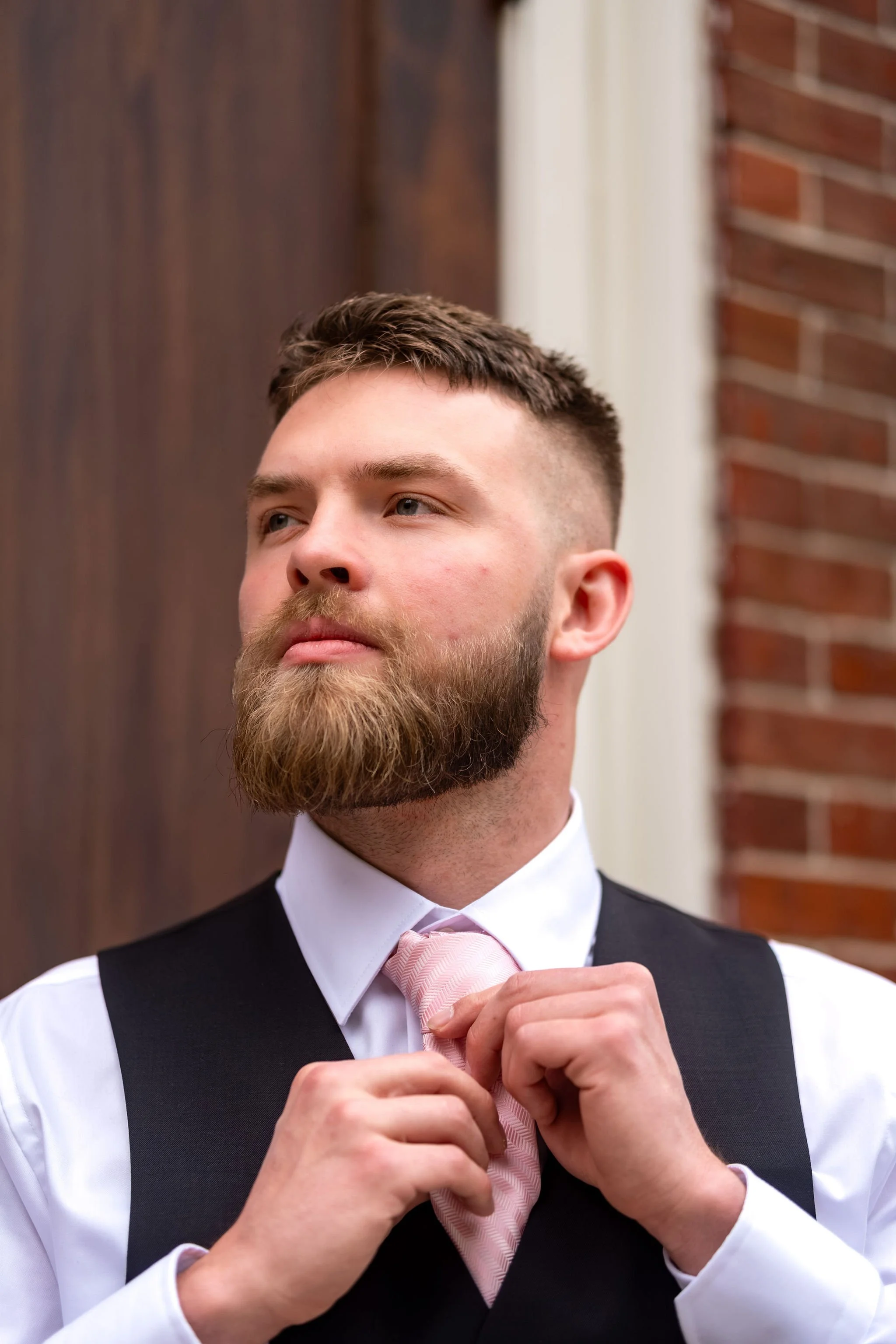 Jeremiah and Vienna close portrait of groom adjusting tie against church doorway at Holy Trinity Greek Orthodox Church Portland Maine spring wedding photography VMG Productions