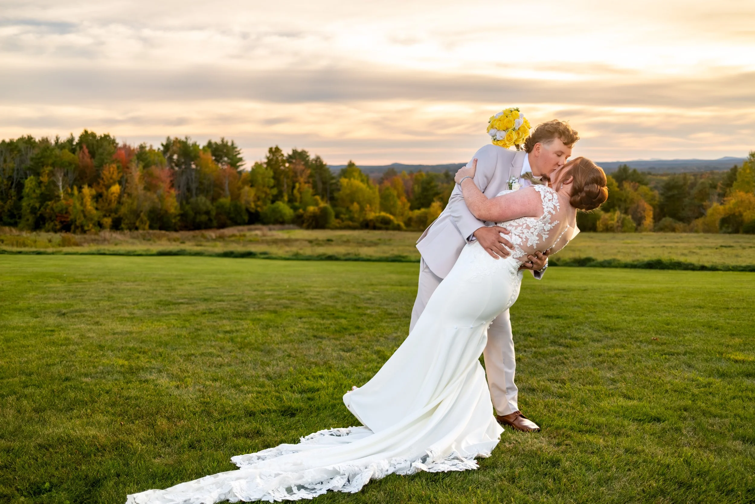 Andrew dipping Erika for a kiss in the field with her long train sweeping the grass at the Maine Wedding Barn and Event Center in Minot Maine fall wedding photography VMG Productions