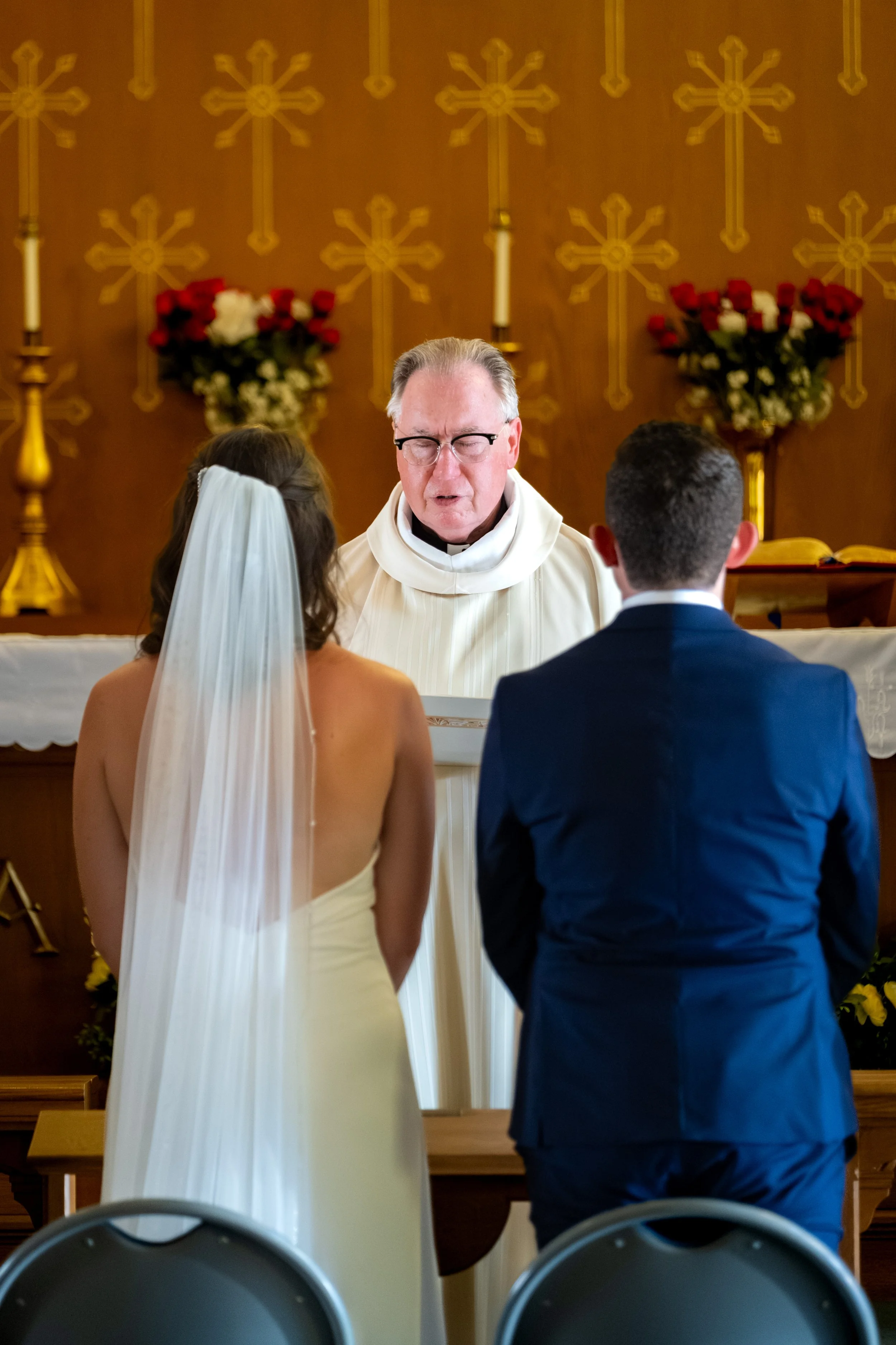 Caroline and Anthony Pirolli standing at the altar with the priest behind them at Star of the Sea in York Maine wedding photography VMG Productions