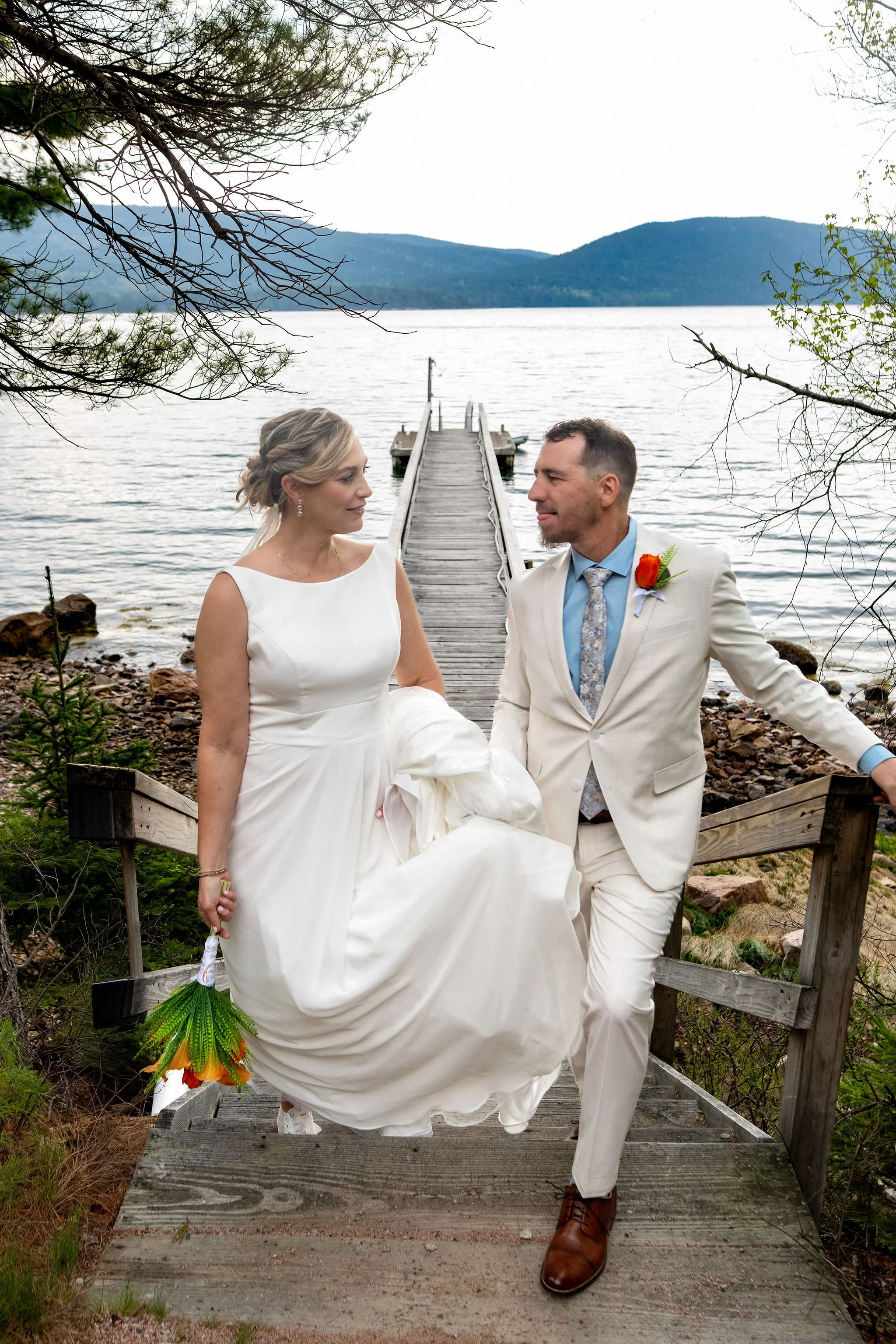 Alli and Adam Baudoin climbing the wooden steps from the dock with the pier and Somes Sound behind them in Mount Desert Maine spring wedding photography VMG Productions