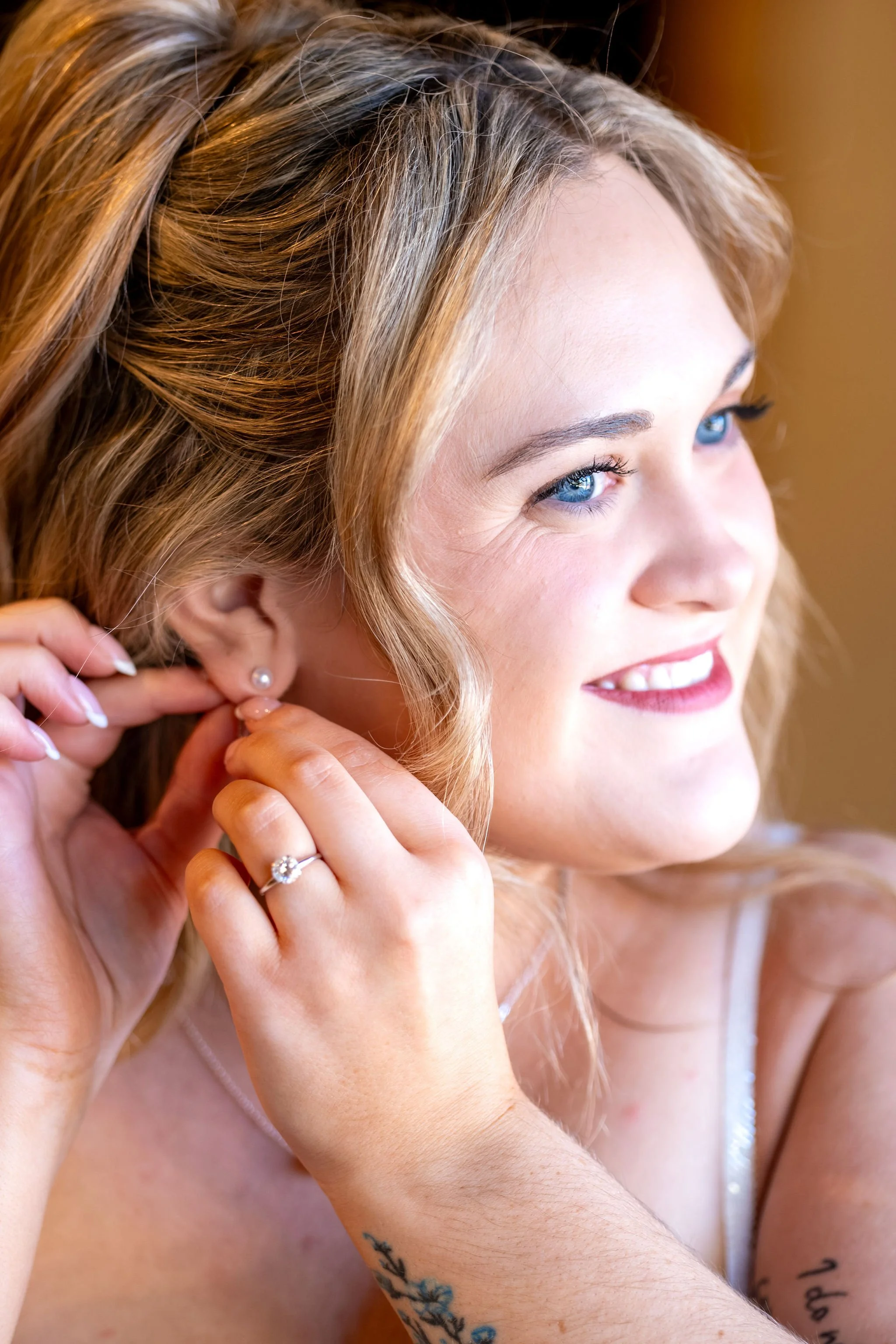 Ellie smiling as she puts in her earring with the sunlight on her face at Boothbay Playhouse in Boothbay Maine fall wedding photography VMG Productions