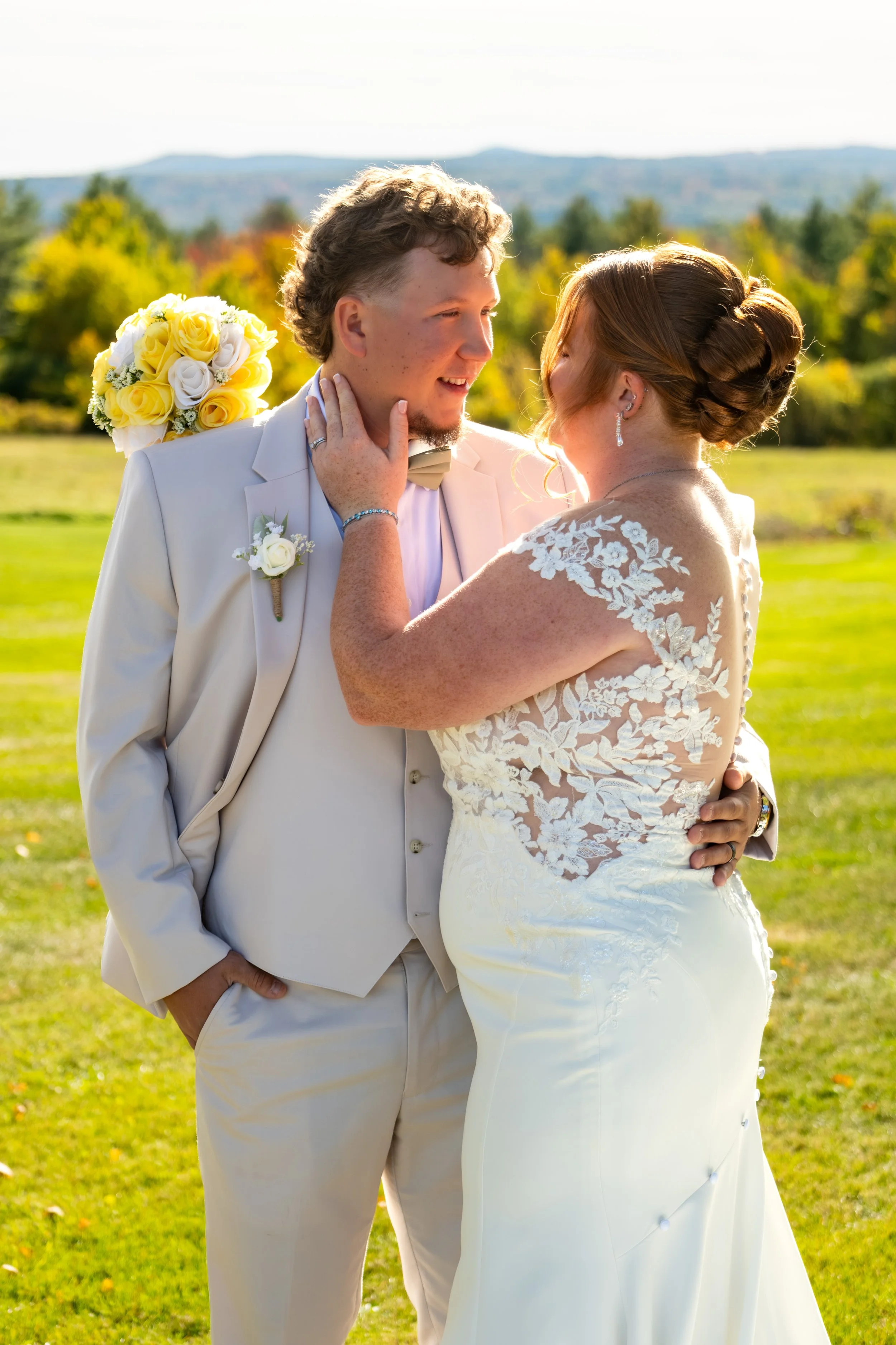 Andrew holding Erika's chin as she smiles with her yellow bouquet at his shoulder at the Maine Wedding Barn and Event Center in Minot Maine fall wedding photography VMG Productions