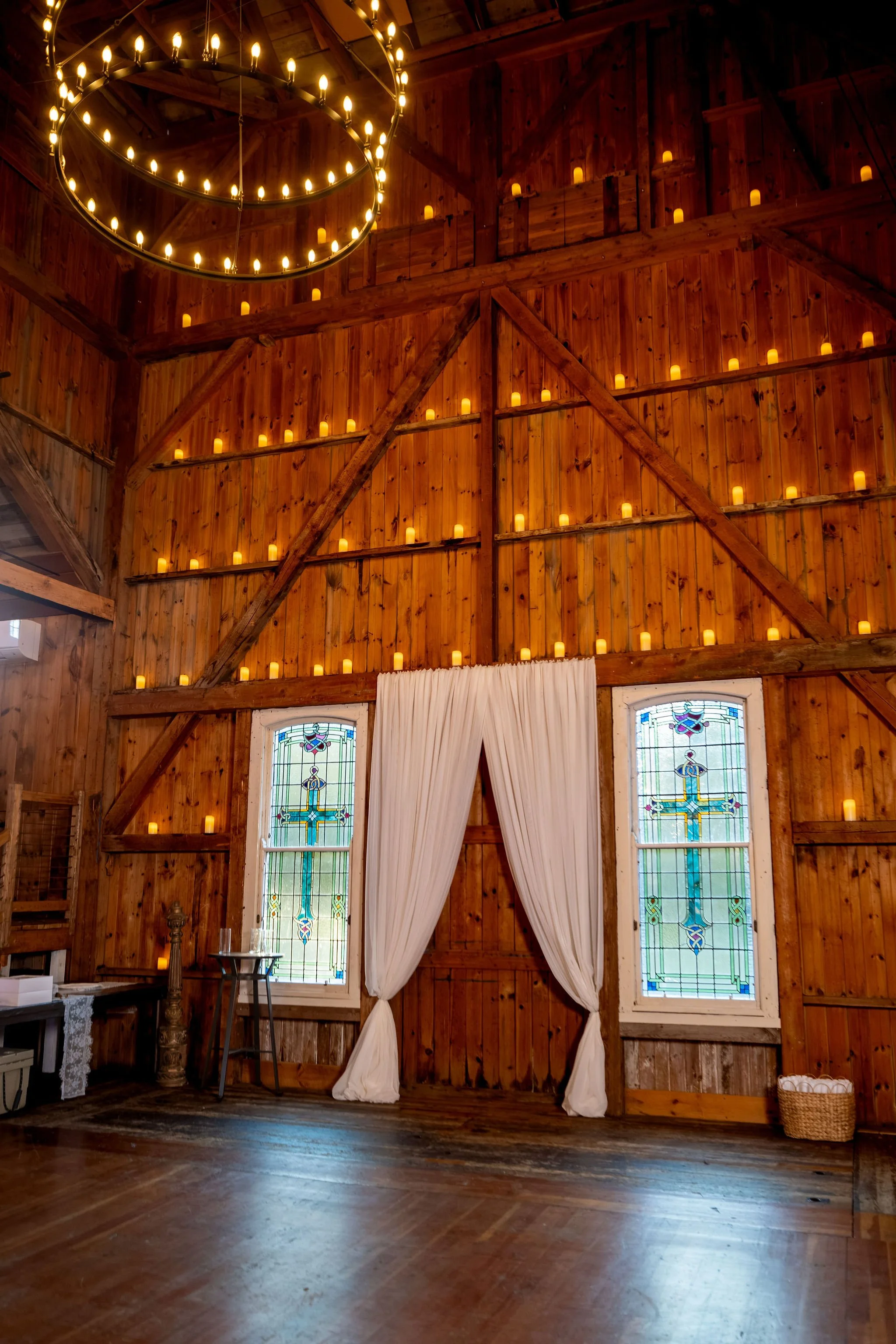 The barn's wooden walls lined with candles above stained glass windows and cream draping at Boothbay Playhouse in Boothbay Maine fall wedding photography VMG Productions