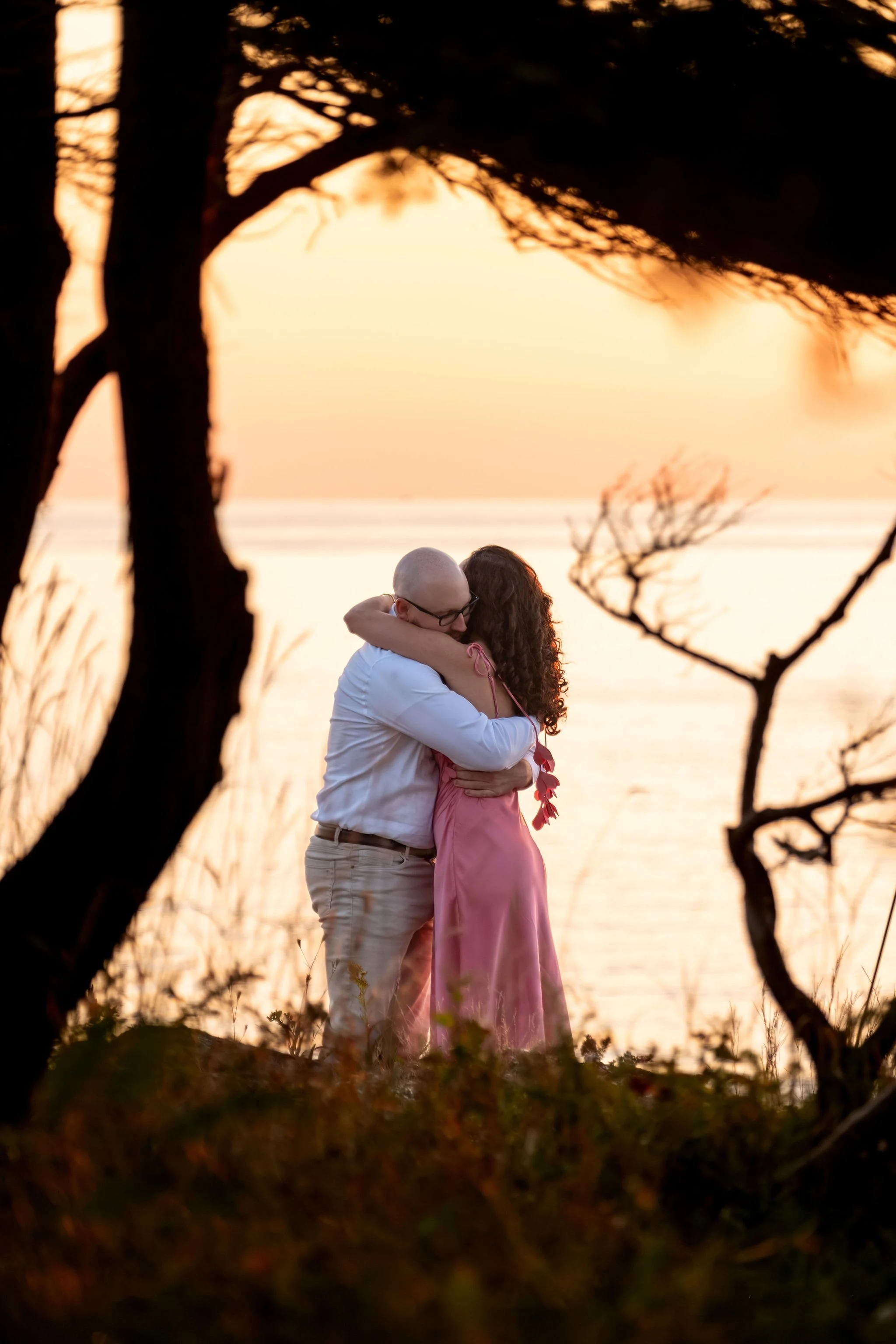 Zack and Helena wrapped in a tight hug against the sunrise sky on Marginal Way in Ogunquit Maine sunrise proposal and engagement photography VMG Productions