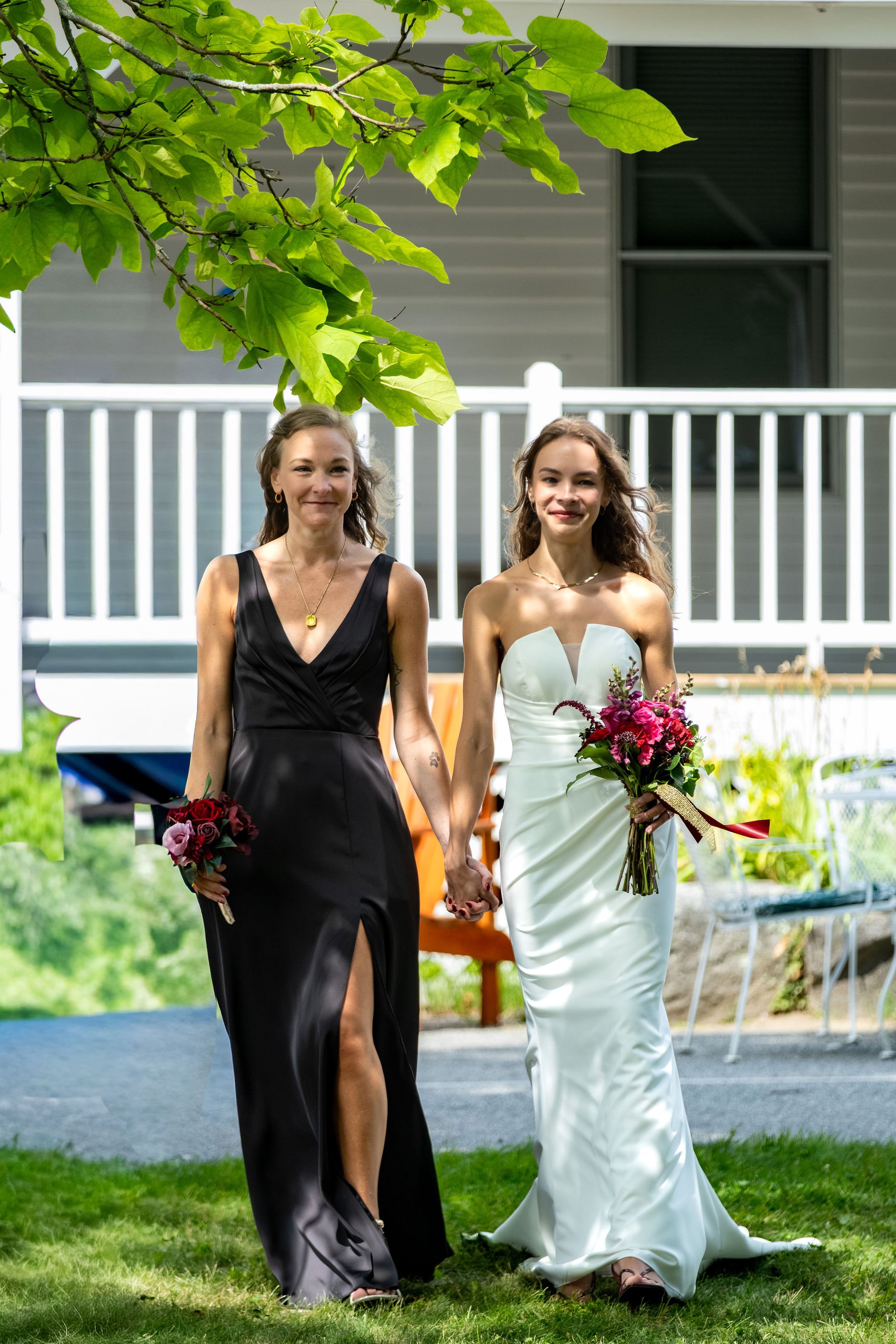 Cassidy Begin walking to the ceremony with her sister carrying a burgundy bouquet at Maple Hill Farm Inn and Conference Center in Hallowell Maine summer wedding photography VMG Productions
