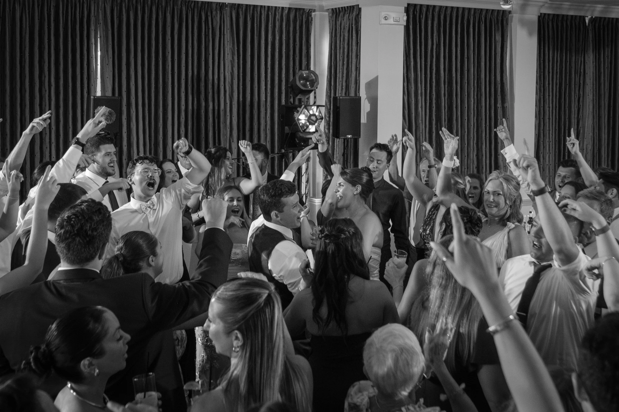 Wedding guests packed on the dance floor with their arms up in black and white at Union Bluff Hotel in York Maine wedding photography VMG Productions