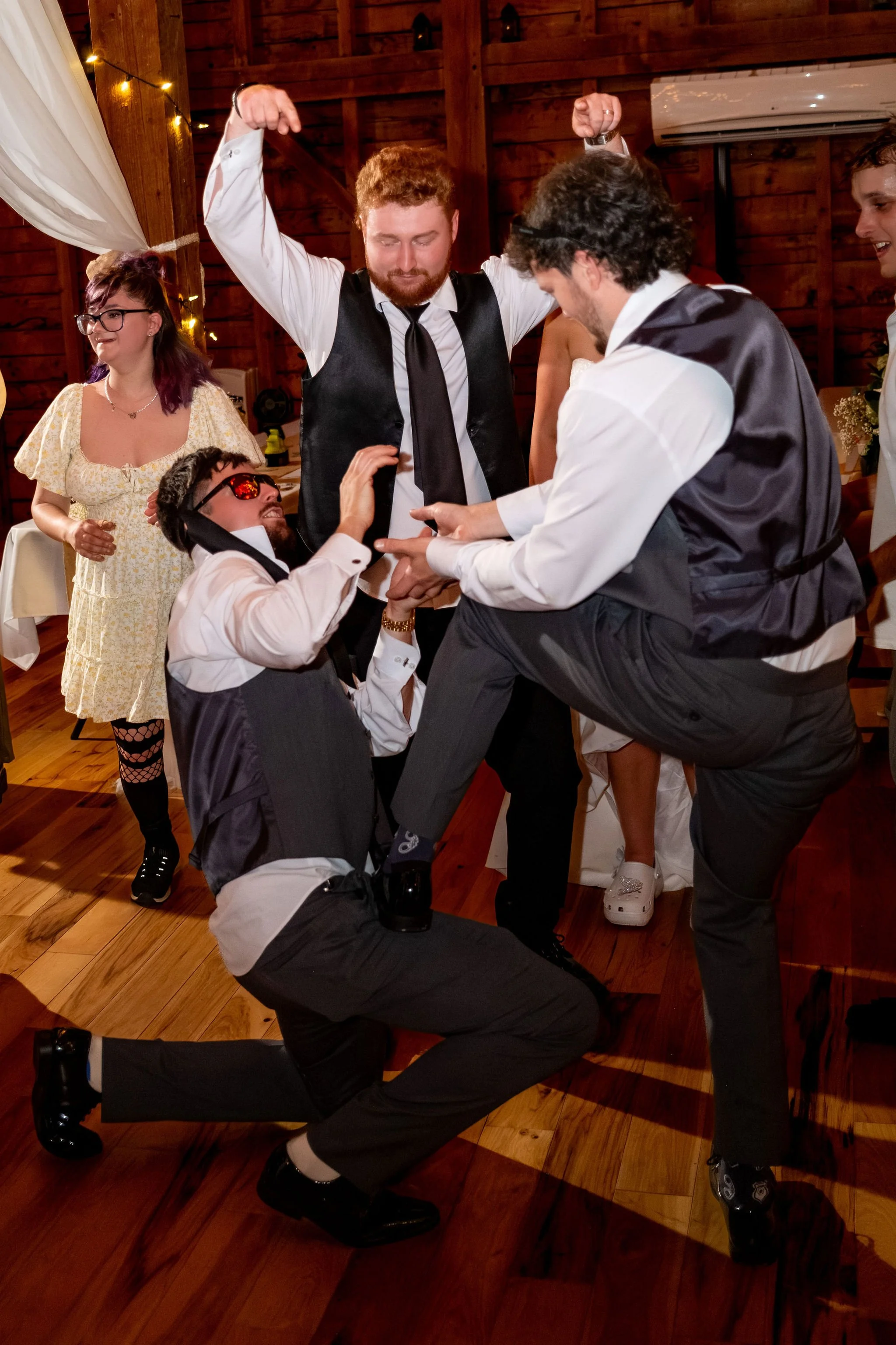 Alyssa and Colby groomsmen goofing around on the dance floor with a tie worn as a headband at the 1888 Barn Bethel Maine summer wedding photography VMG Productions