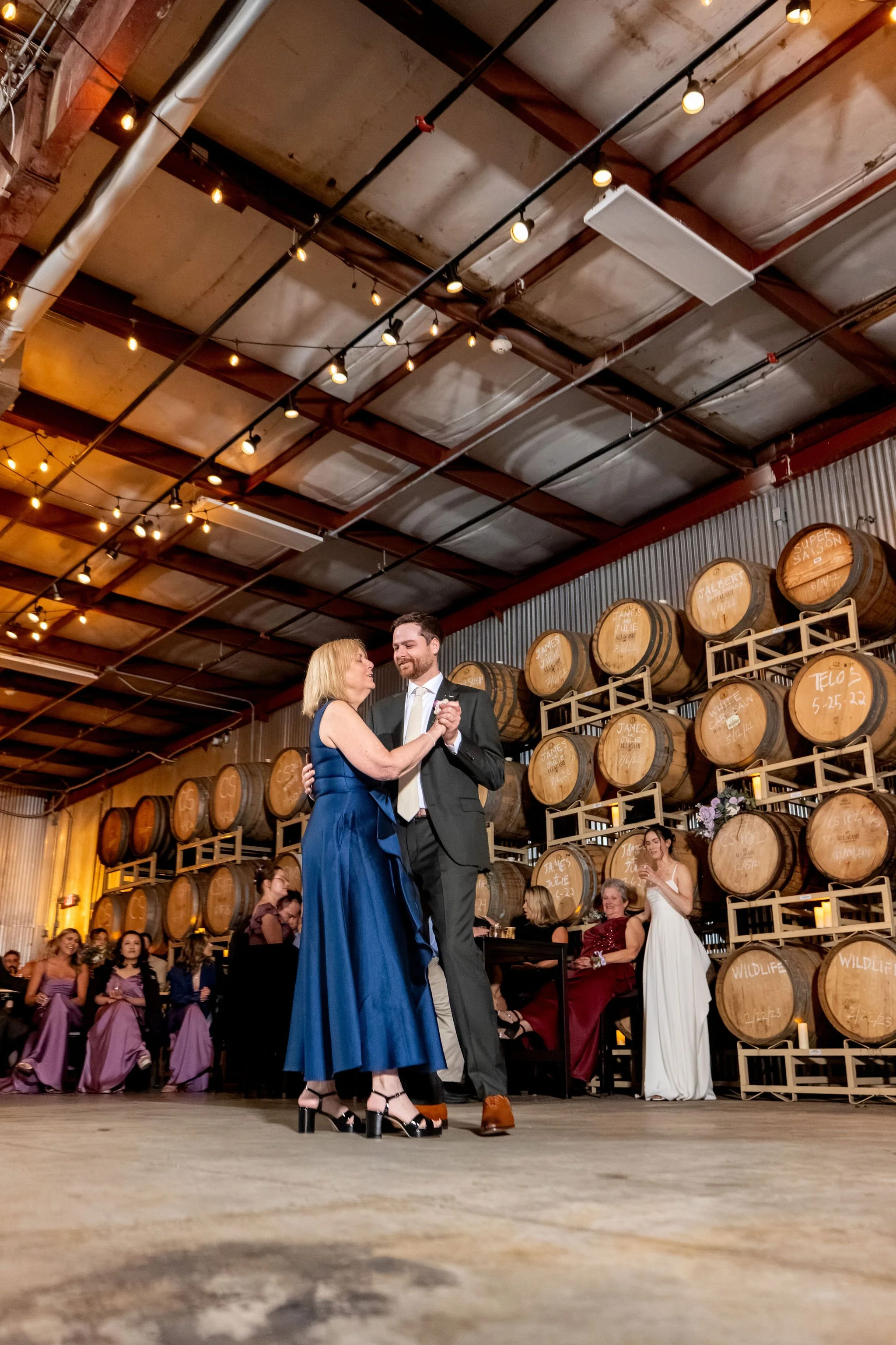 Jack dancing with his mom in a blue gown on the barrel room floor at The Cellars at Allagash Brewing Company in Portland Maine fall wedding photography VMG Productions