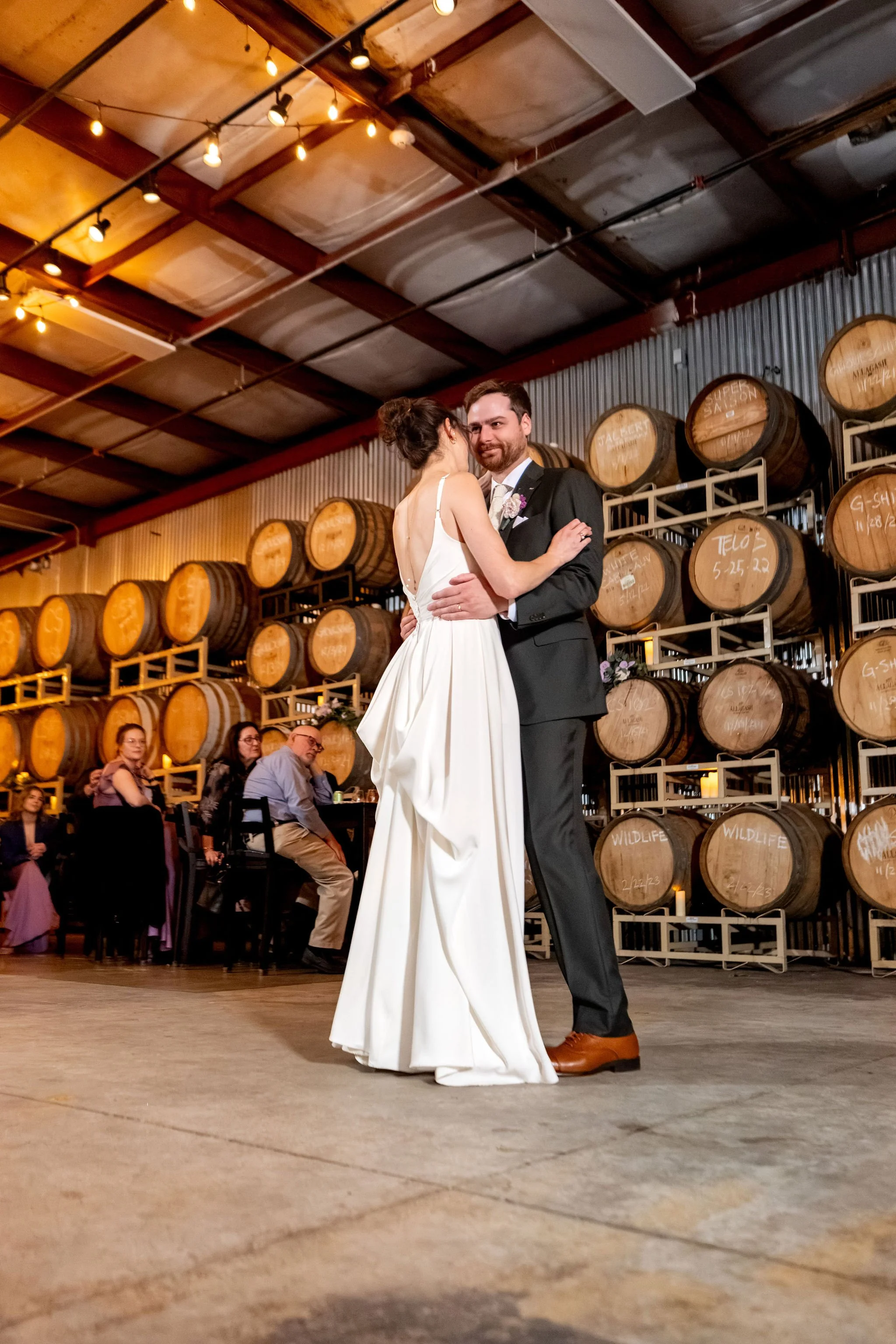 Victoria and Jack's first dance in the barrel room under string lights at The Cellars at Allagash Brewing Company in Portland Maine fall wedding photography VMG Productions