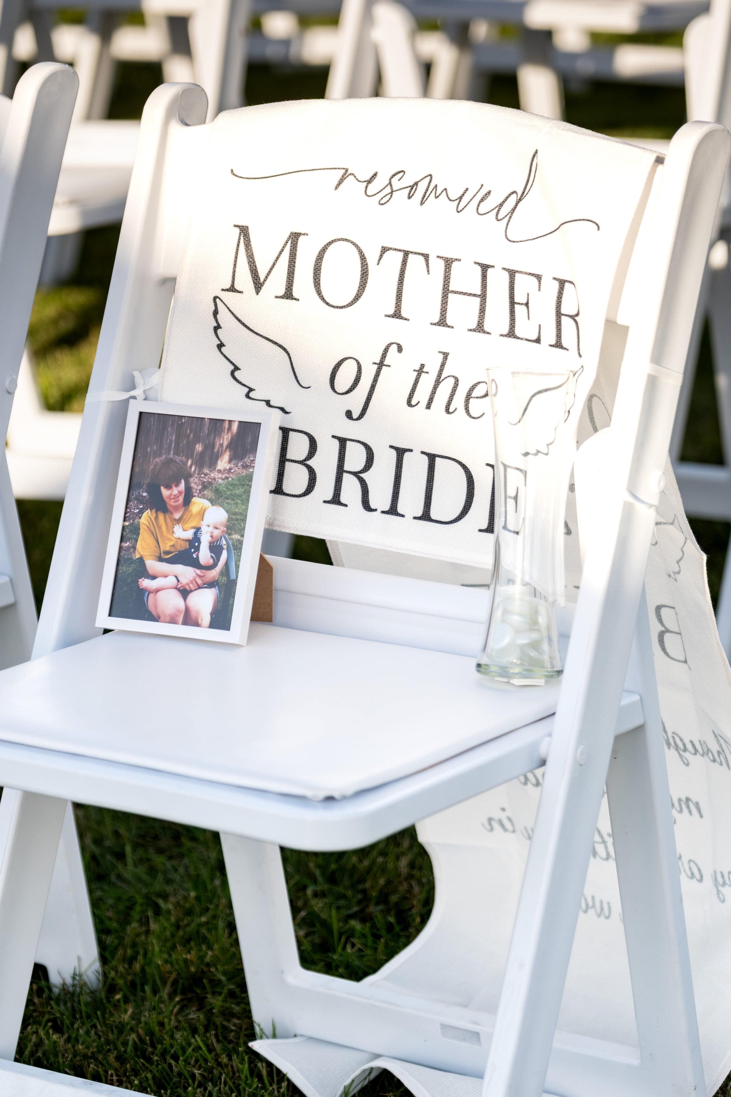 A reserved white chair in memory of the mother of the bride, with her framed photo and a vase on the seat at the Maine Wedding Barn and Event Center in Minot Maine fall wedding photography VMG Productions