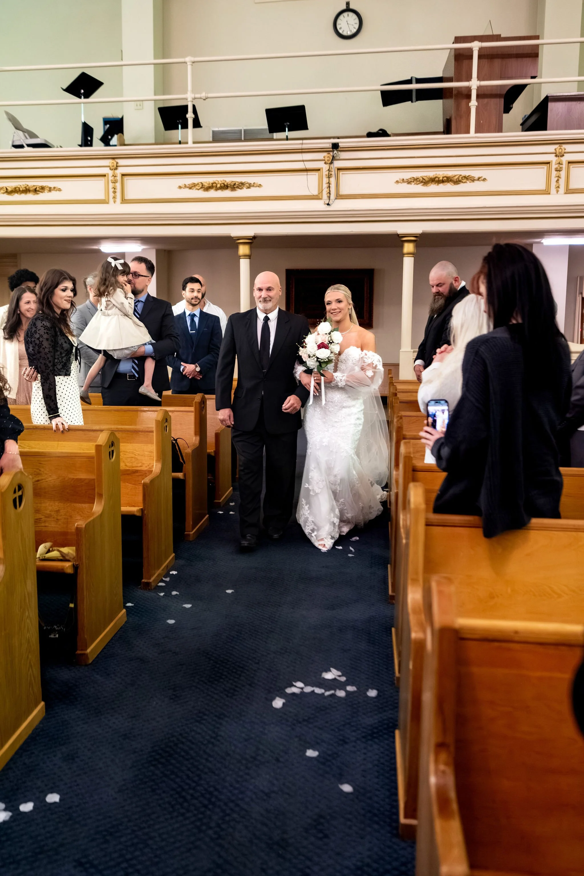 Jeremiah and Vienna bride escorted down aisle by her father as guests look on at Holy Trinity Greek Orthodox Church Portland Maine spring wedding photography VMG Productions