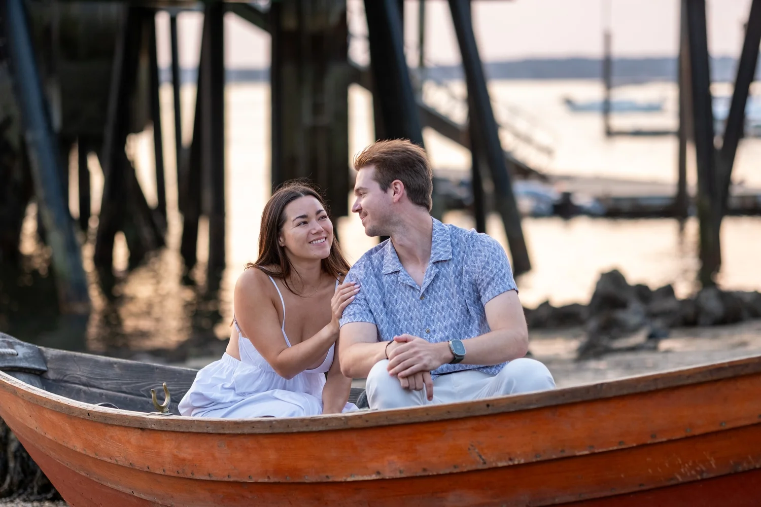 Couple sitting in a wooden dinghy under the pier, Peaks Island, Portland, Maine, by VMG Productions
