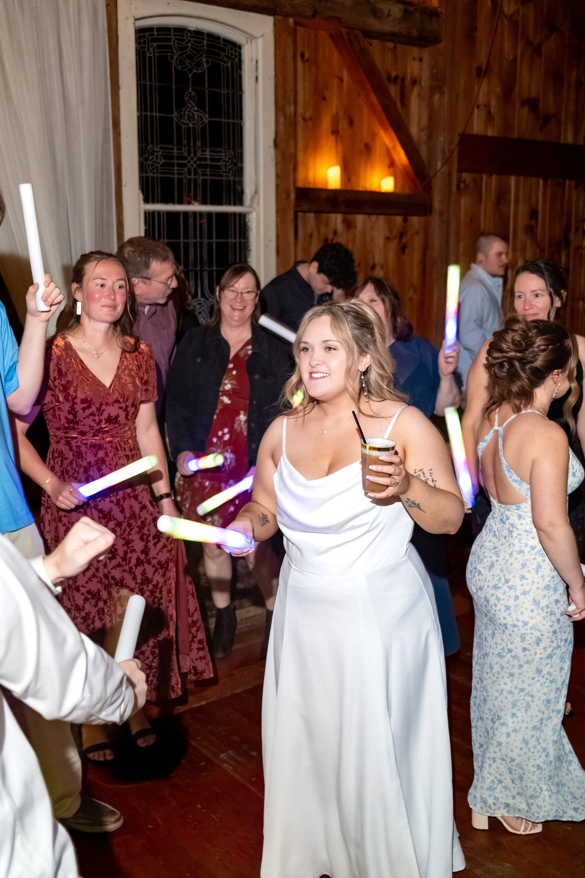 Ellie dancing in a white slip dress with a drink in her hand and friends dancing with glow sticks around her at Boothbay Playhouse in Boothbay Maine fall wedding photography VMG Productions