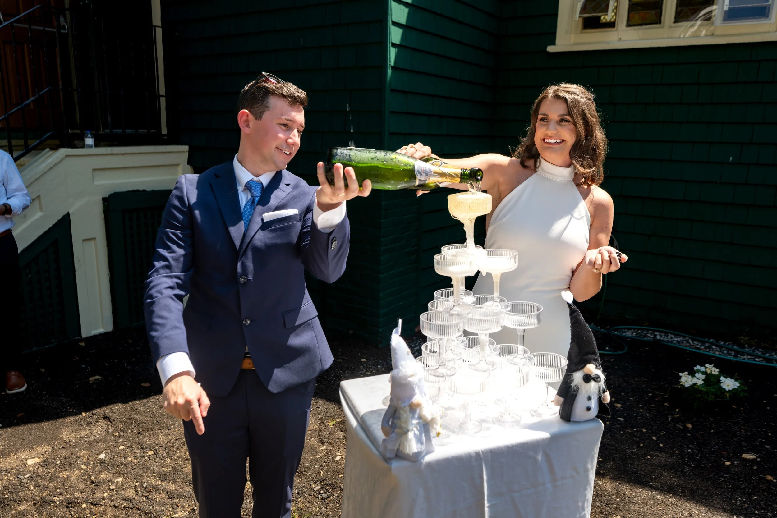 Caroline and Anthony Pirolli pouring the champagne tower outside the green shingle walls of Star of the Sea in York Maine wedding photography VMG Productions