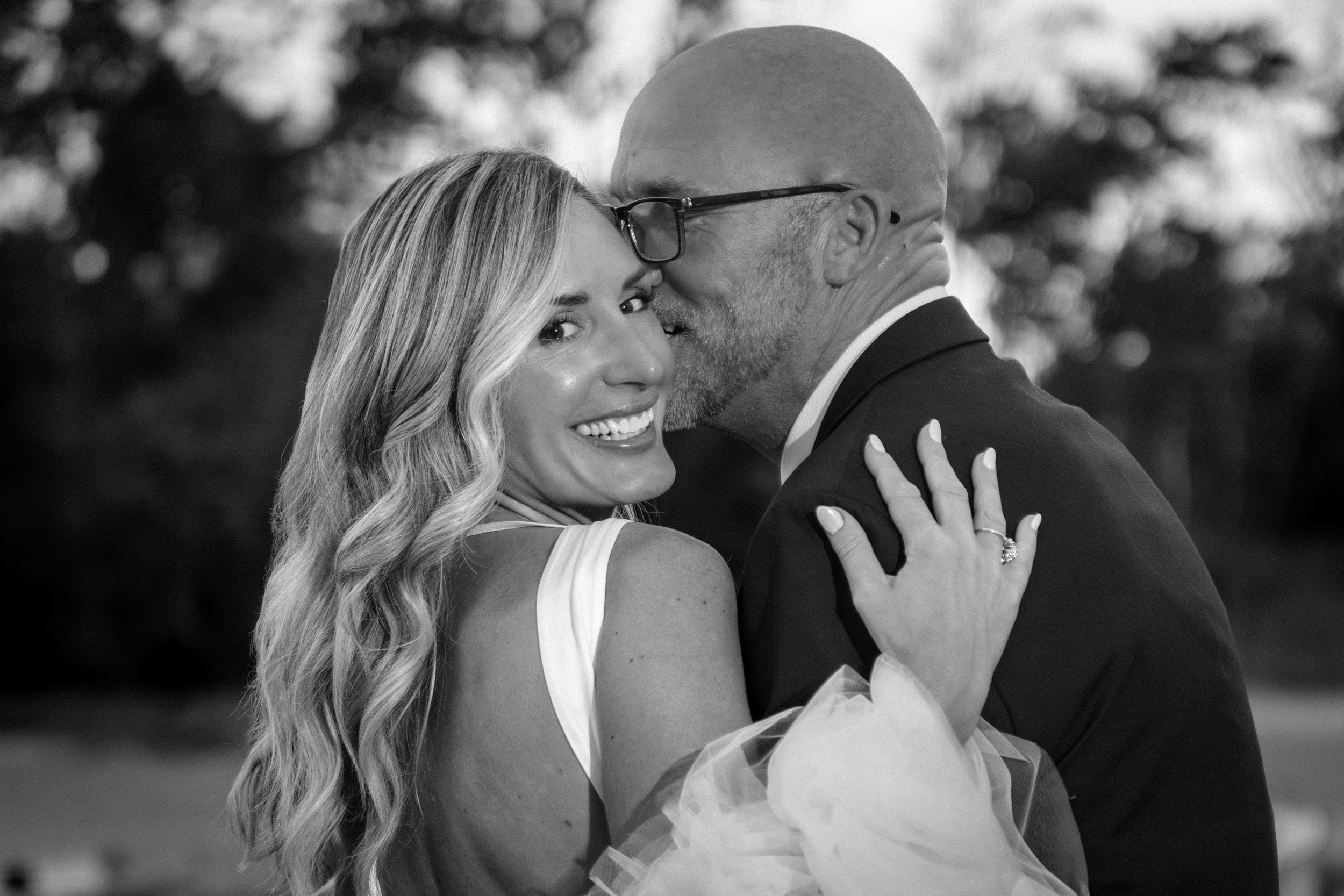Marc Draper stealing a kiss on the cheek as Ashley smiles at golden hour in black and white at The Breakwater Inn in Kennebunkport Maine summer wedding photography VMG Productions