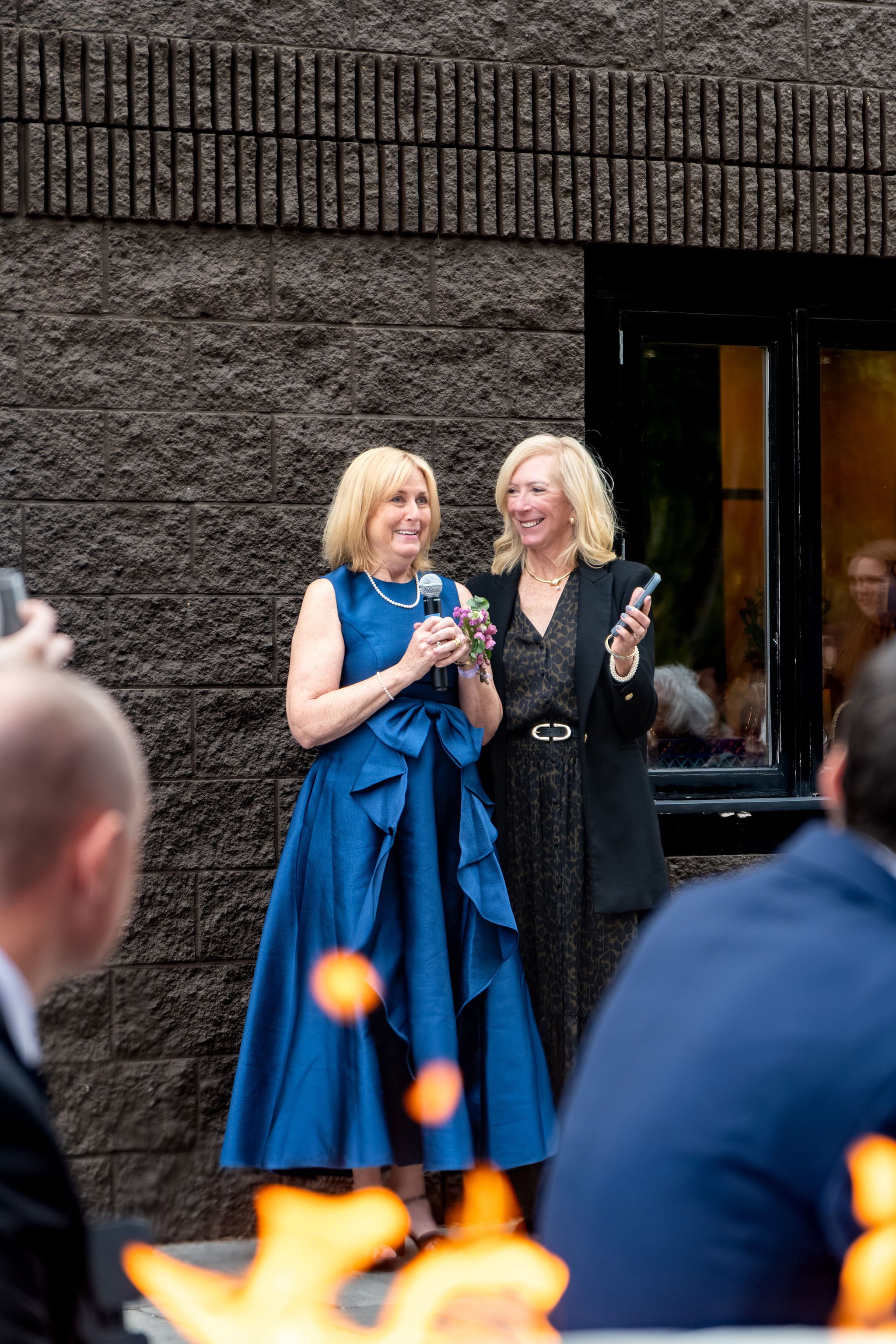 Jack's mom in a blue gown laughing as she gives a toast on the patio at The Cellars at Allagash Brewing Company in Portland Maine fall wedding photography VMG Productions
