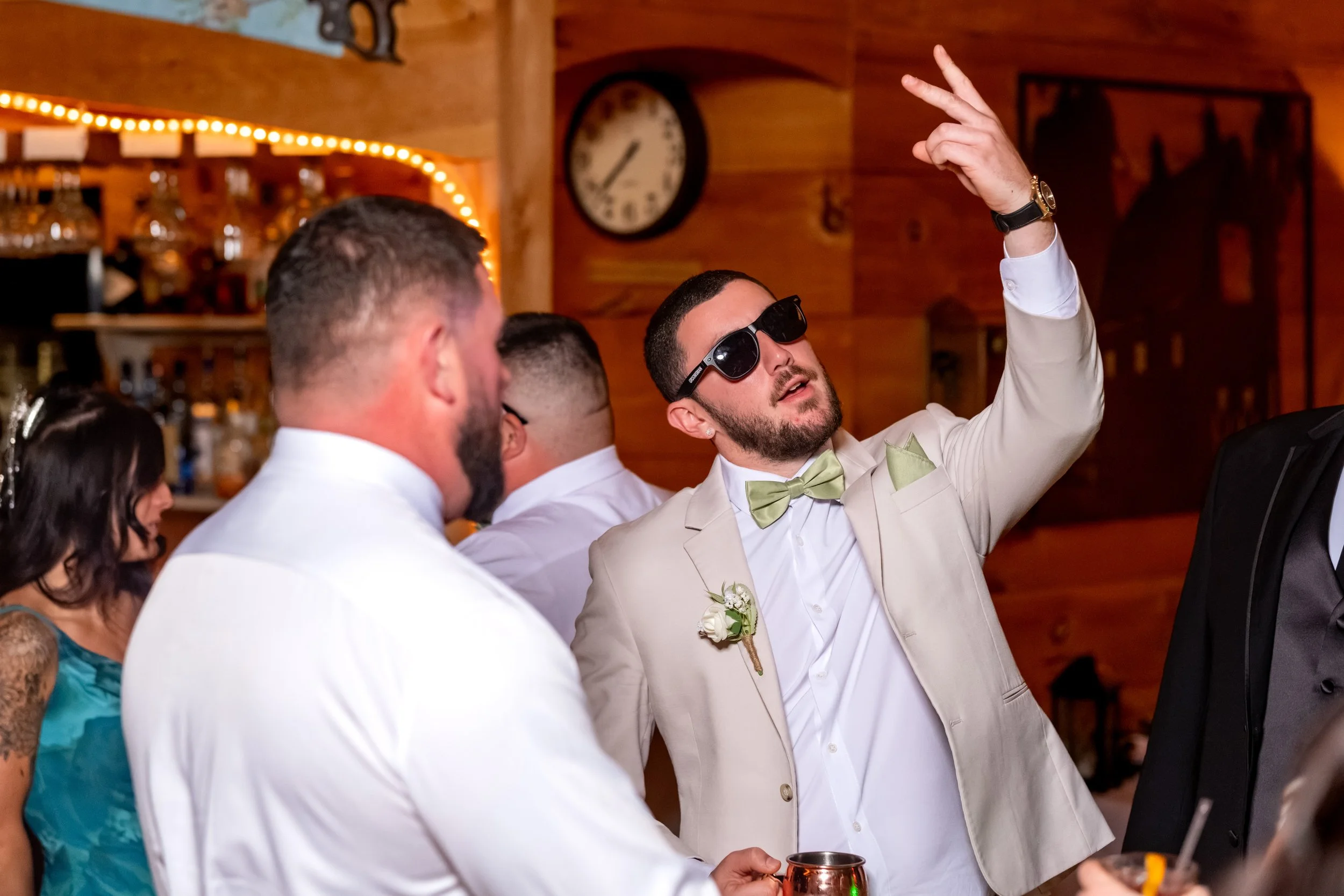 Andrew in sunglasses and a tan suit with his arm raised as he dances with a friend at the Maine Wedding Barn and Event Center in Minot Maine fall wedding photography VMG Productions