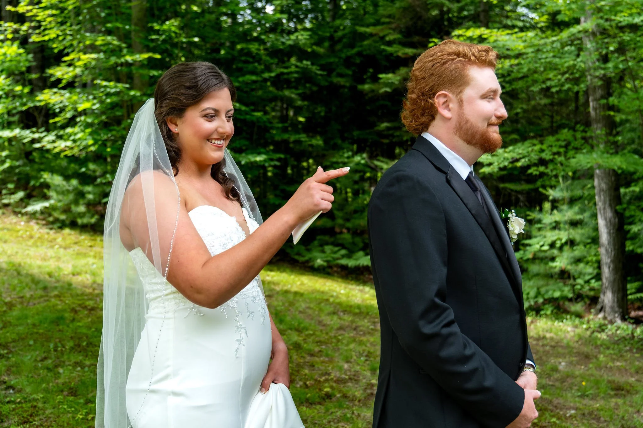 Alyssa and Colby the bride pointing playfully at the groom's back moments before their first look in the woods in Bethel Maine summer wedding photography VMG Productions