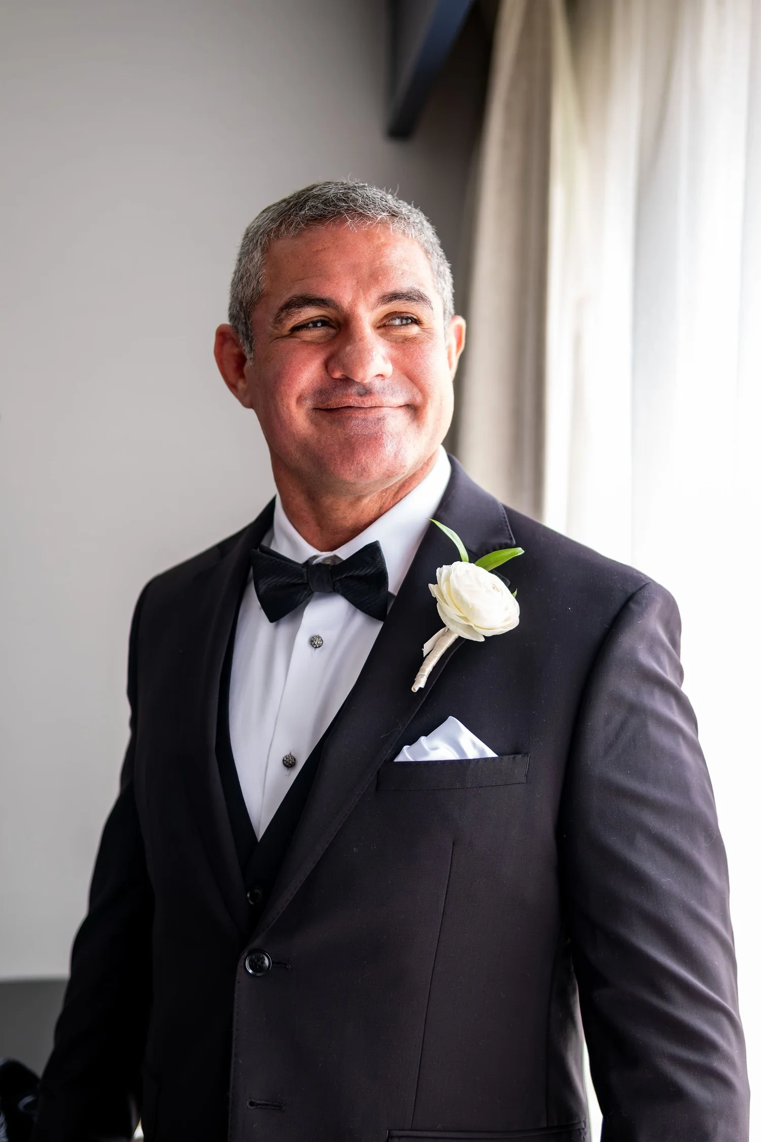Alexey smiling in his tuxedo with white ranunculus boutonniere at Portland Sheraton at Sable Oaks South Portland Maine summer wedding photography VMG Productions