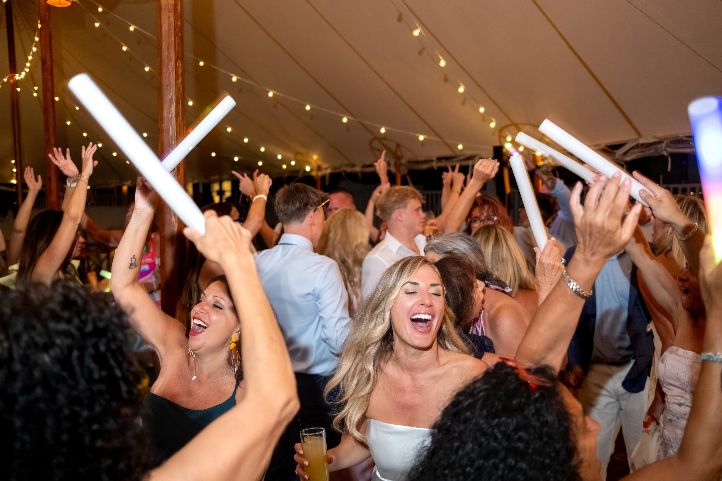 Ashley Draper laughing in the middle of the dance floor as guests raise glow batons around her at The Breakwater Inn in Kennebunkport Maine summer wedding photography VMG Productions